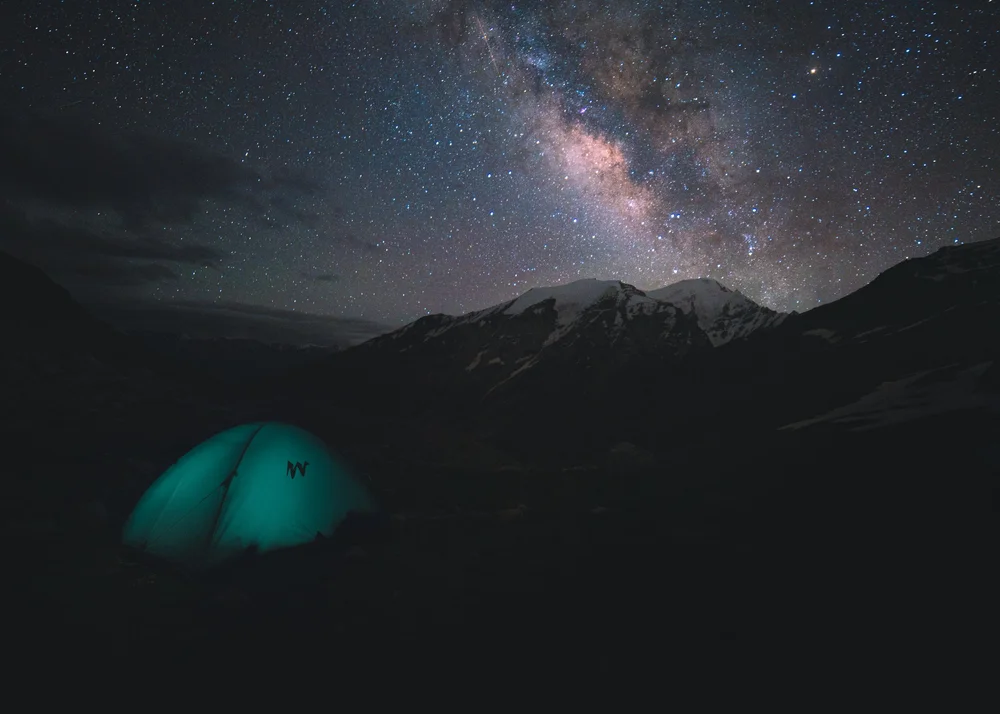A green tent glowing under the Milky Way in the high Himalaya