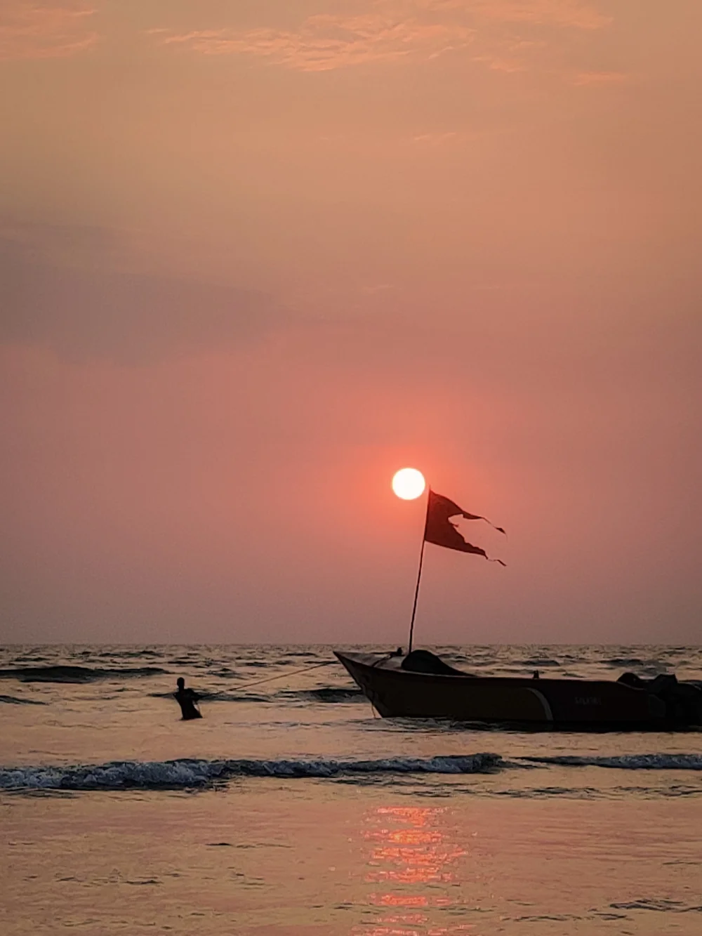 The setting sun beside a flag on a fishing boat, a swimmer in the waves