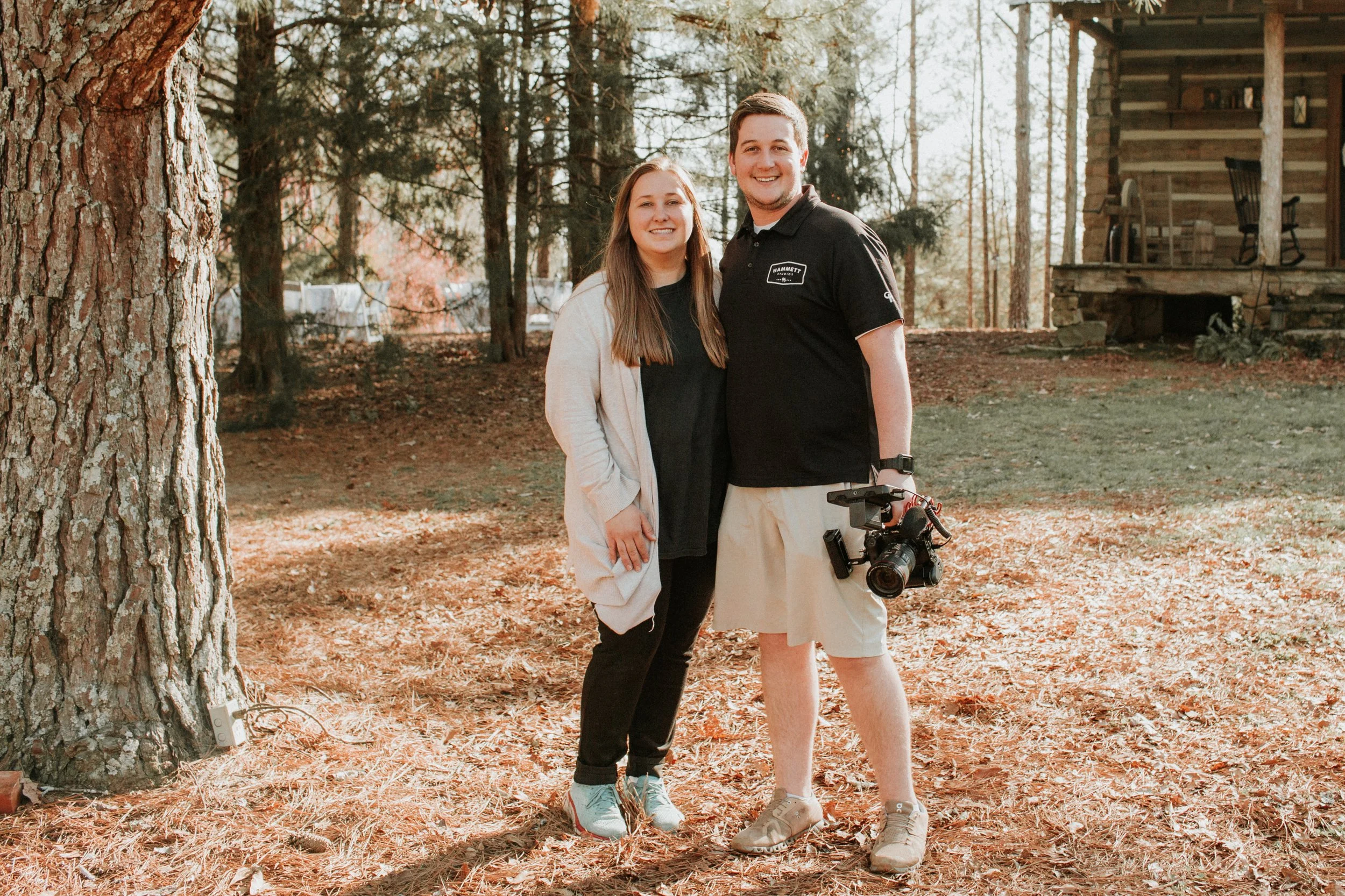 A videographer filming a white wedding dress hung from a tree branch.