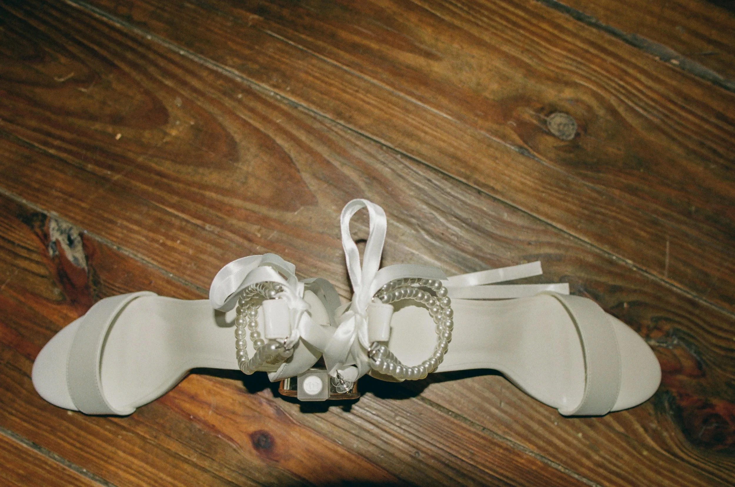 A white garter with decorative pearls, ribbons, and bows, laying on a wooden surface on 35mm film