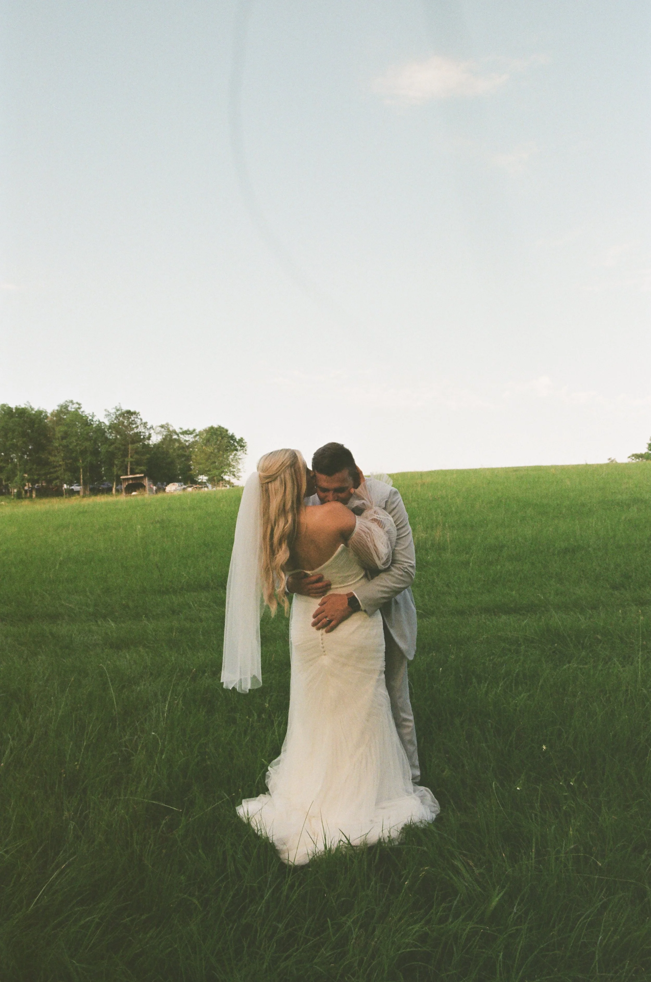 A bride and groom embracing and smiling on a grassy field during their wedding.