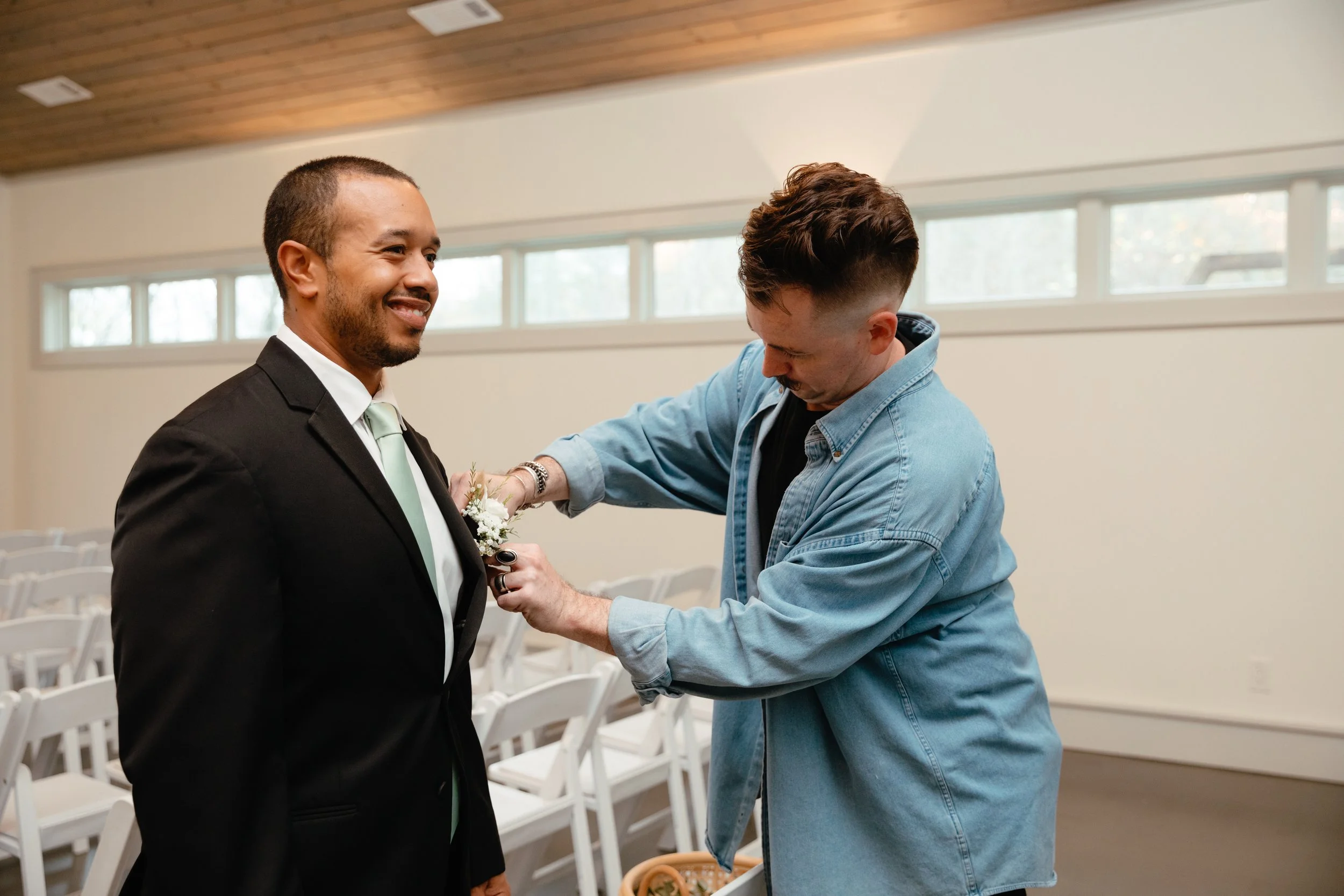 A couple sitting on a vintage cushion in front of a yellow camper van, with a floral arrangement and decorative pillows nearby, in a rural outdoor setting.