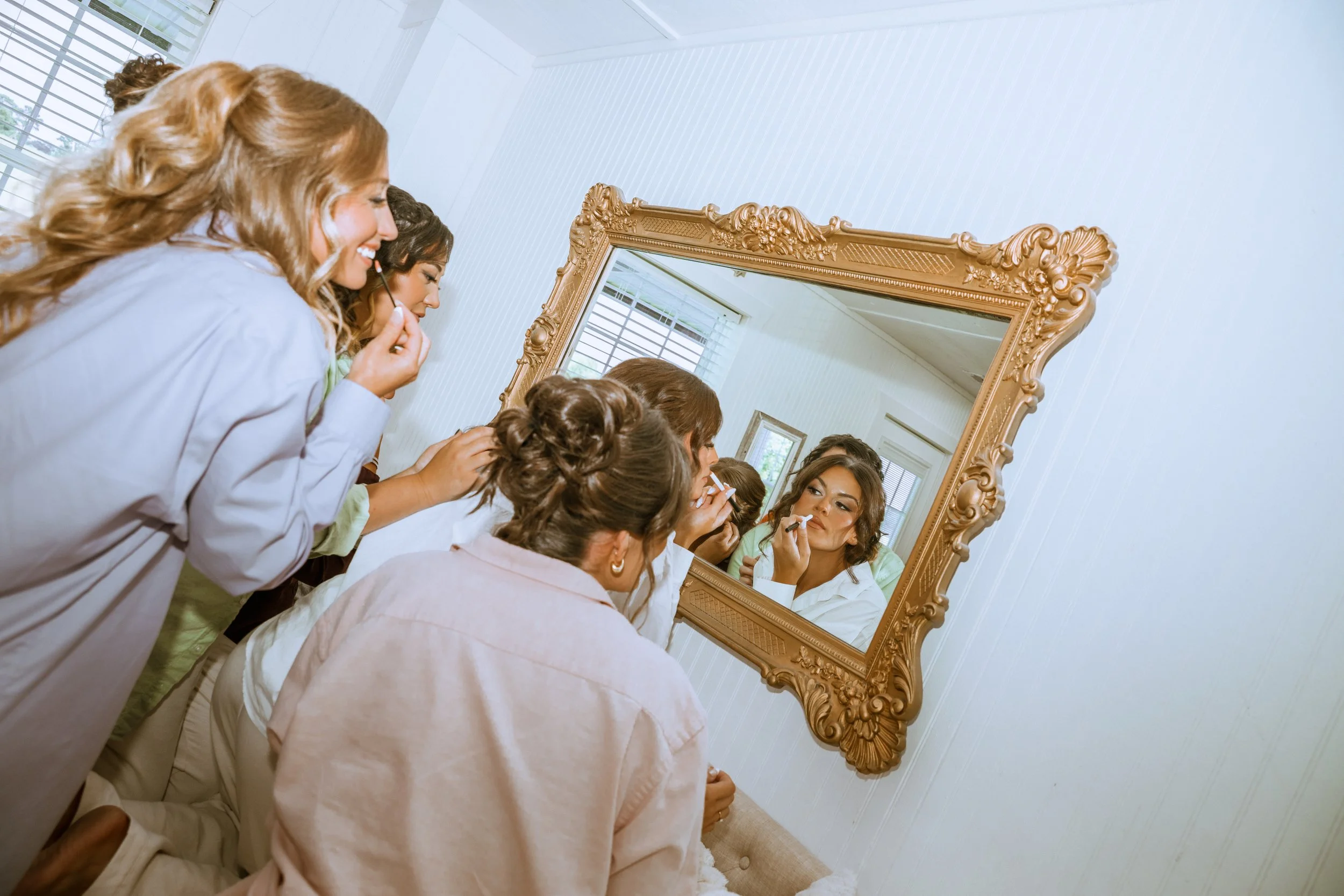 Women looking at themselves in a mirror as part of a hair or makeup session.