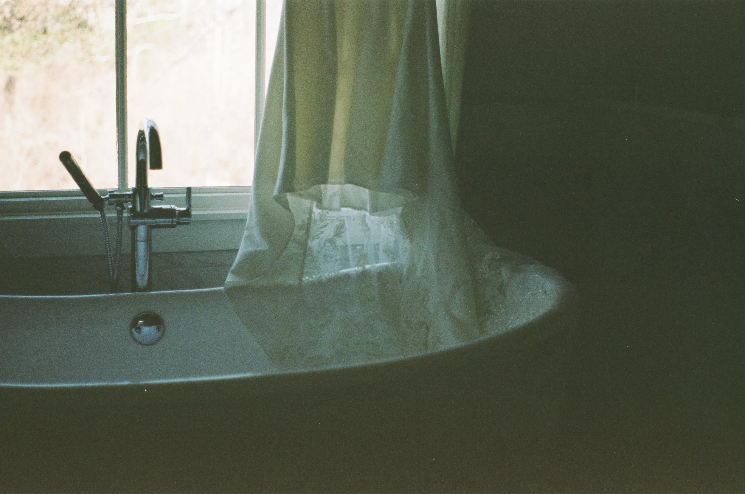 A kitchen sink with a window above it and a curtain hanging partially over the sink.