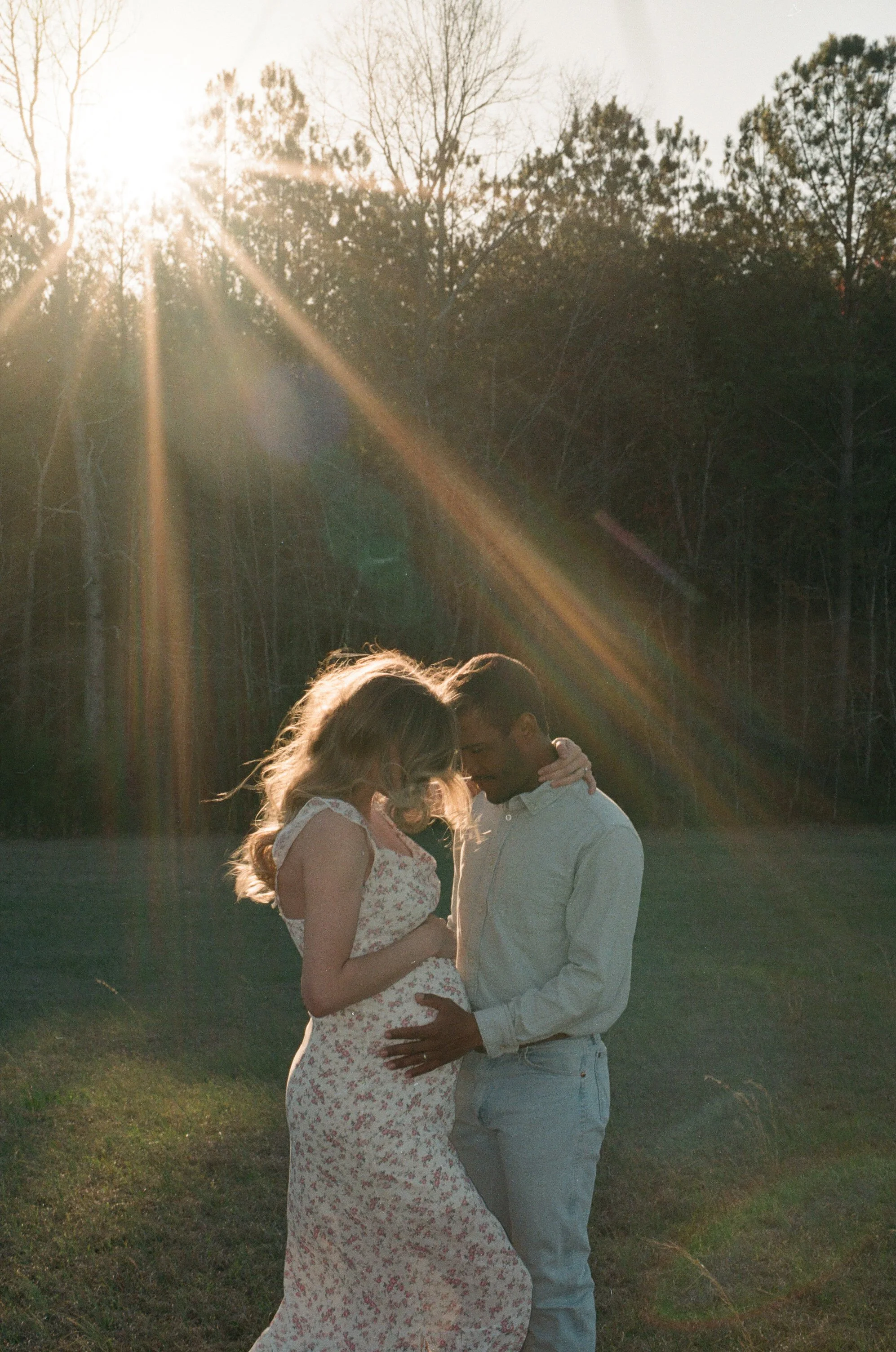 A couple sharing an intimate moment outdoors during sunset, with the sun's rays shining down on them at the back 40 farm in jacksonville, alabama on riley green's venue on 35mm film