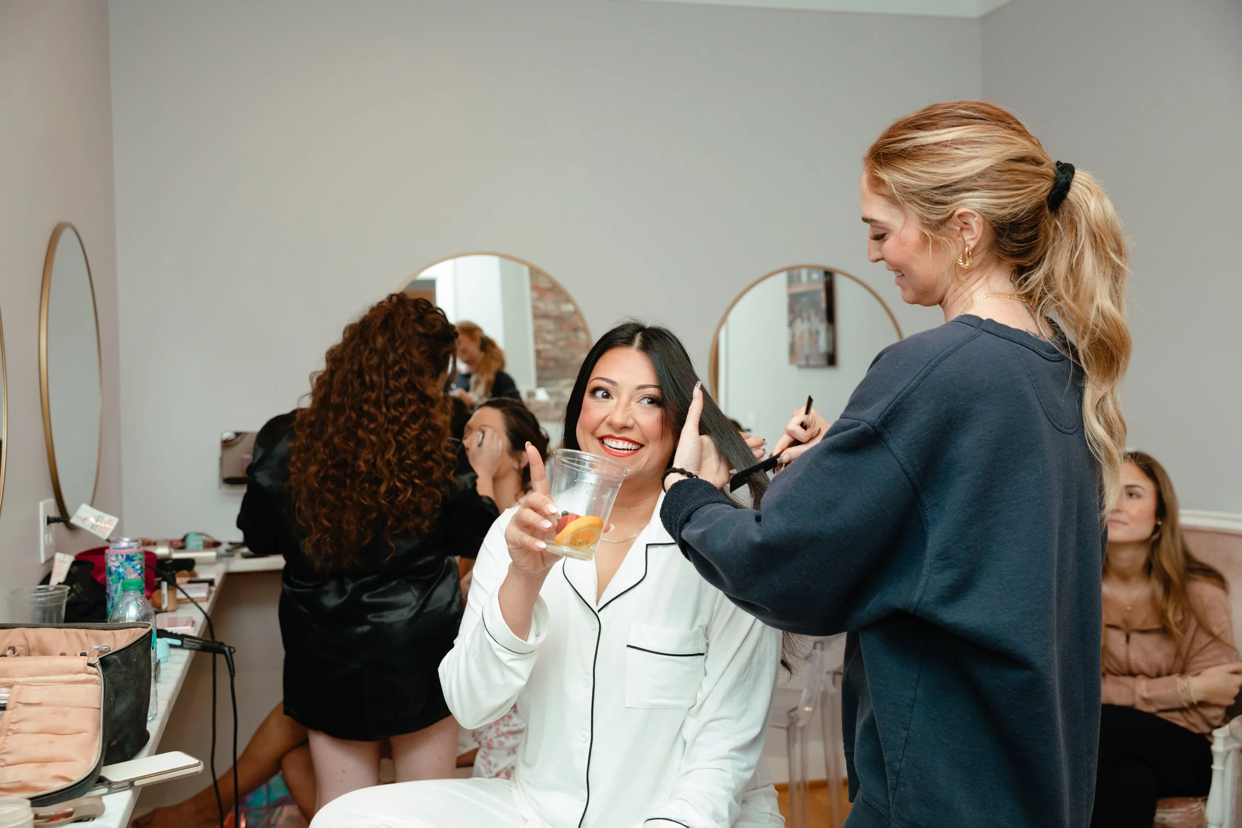 A woman with styled hair smiling while a stylist works on her hair in a decorated room.