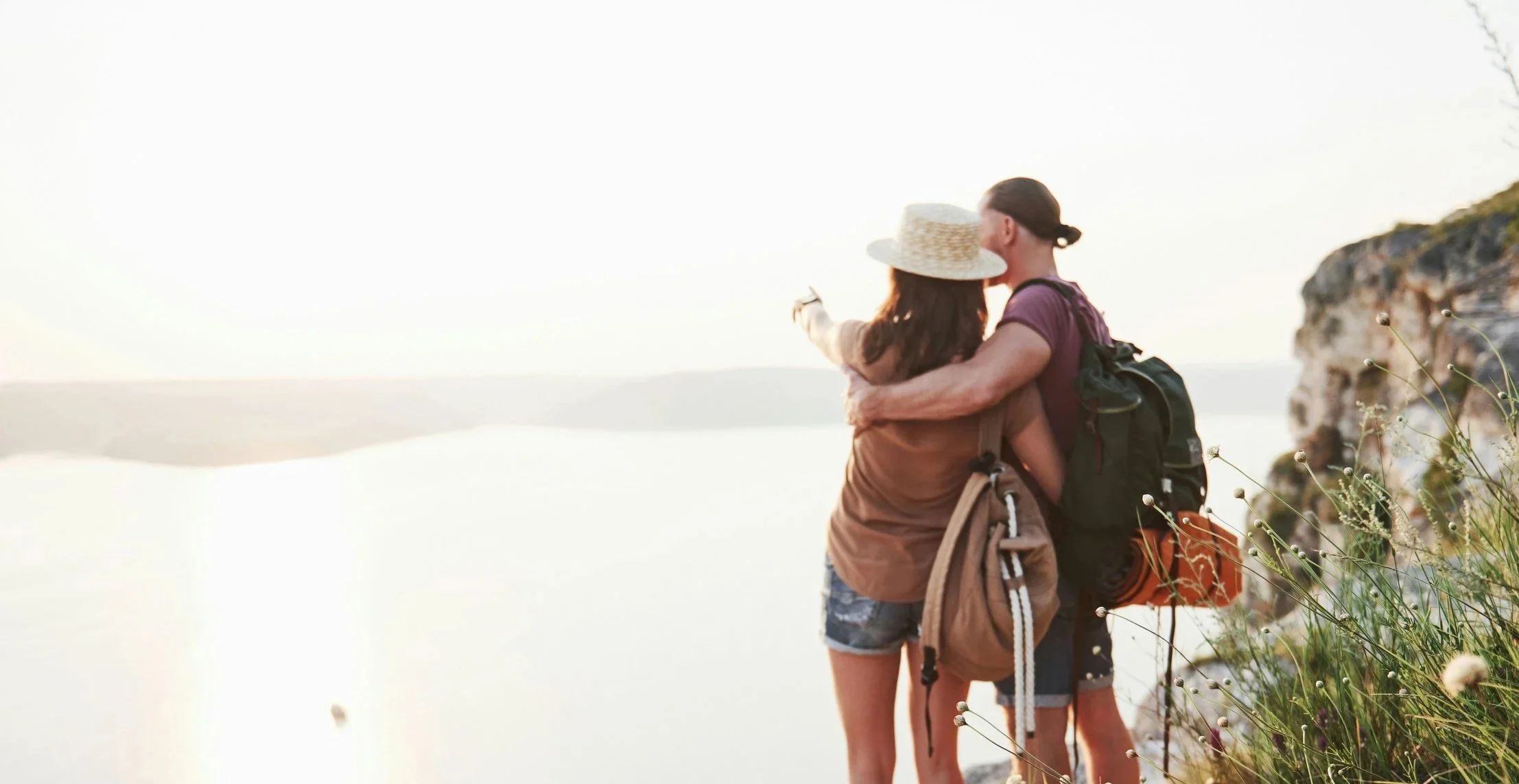 Couple with backpacks standing on a scenic cliff edge overlooking the water while planning a custom travel itinerary.