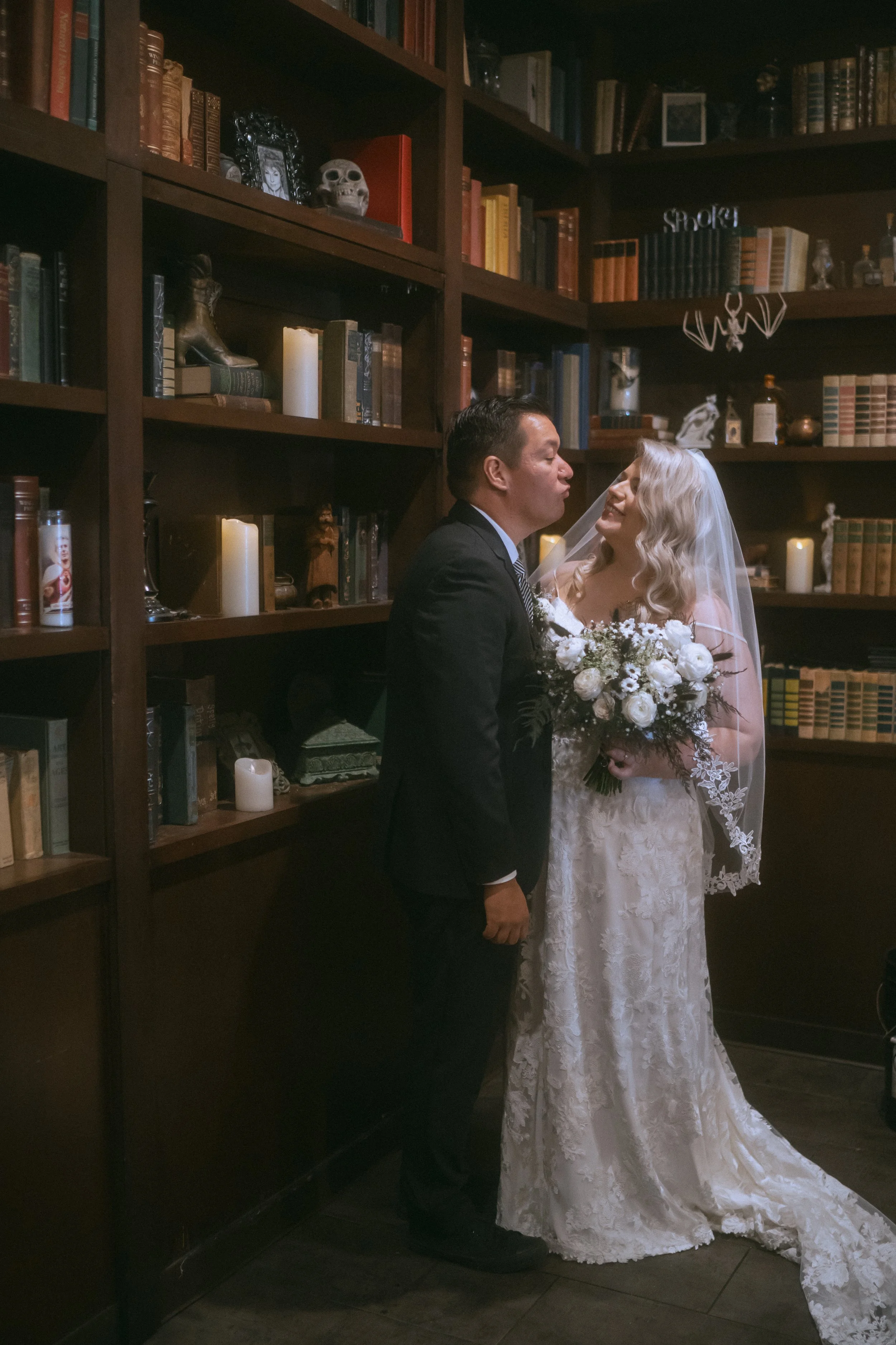 Bride and groom standing in a candlelit library surrounded by bookshelves for a moody, romantic wedding portrait