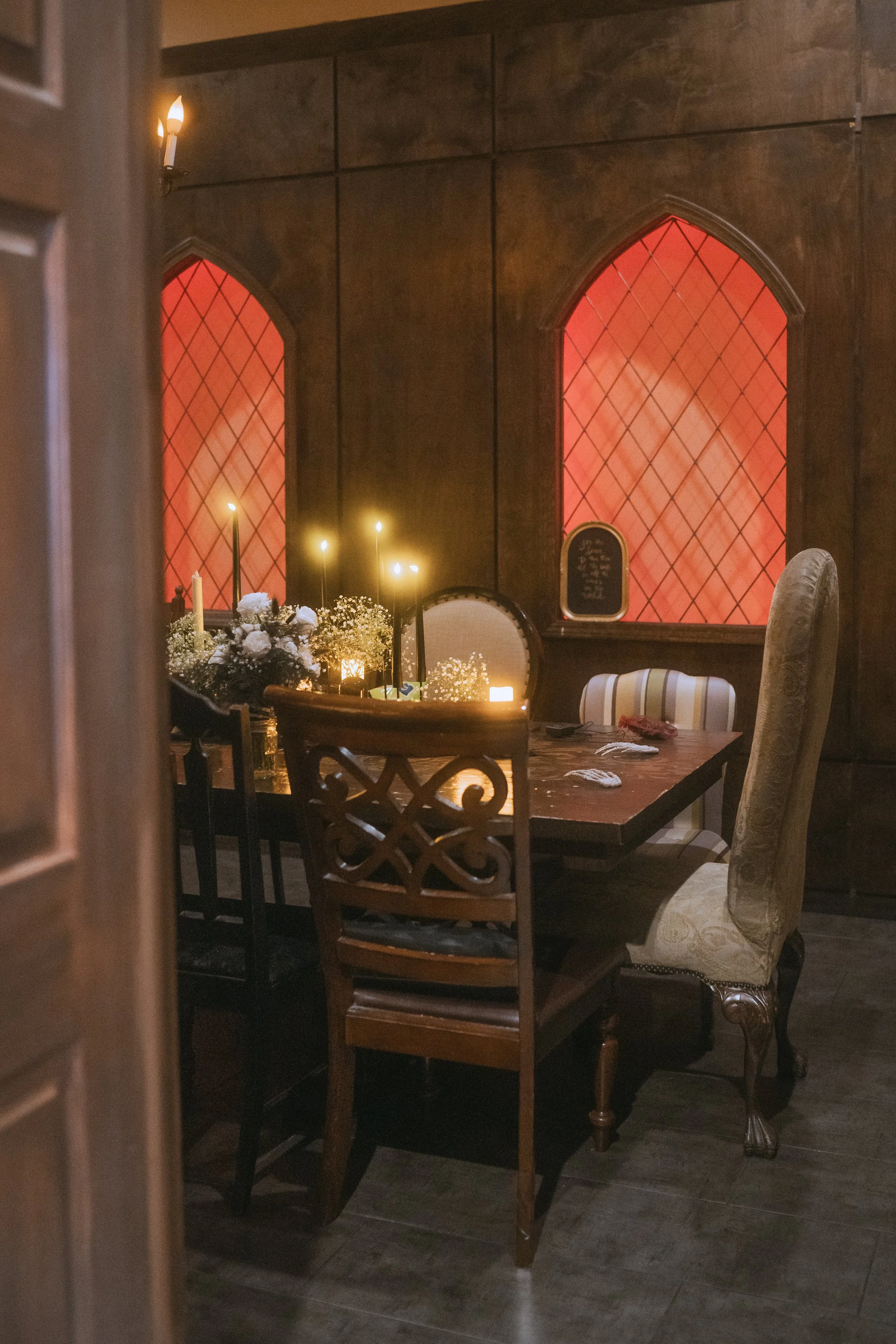 Candlelit wedding table set in front of red stained glass-style windows with vintage chairs and romantic decor