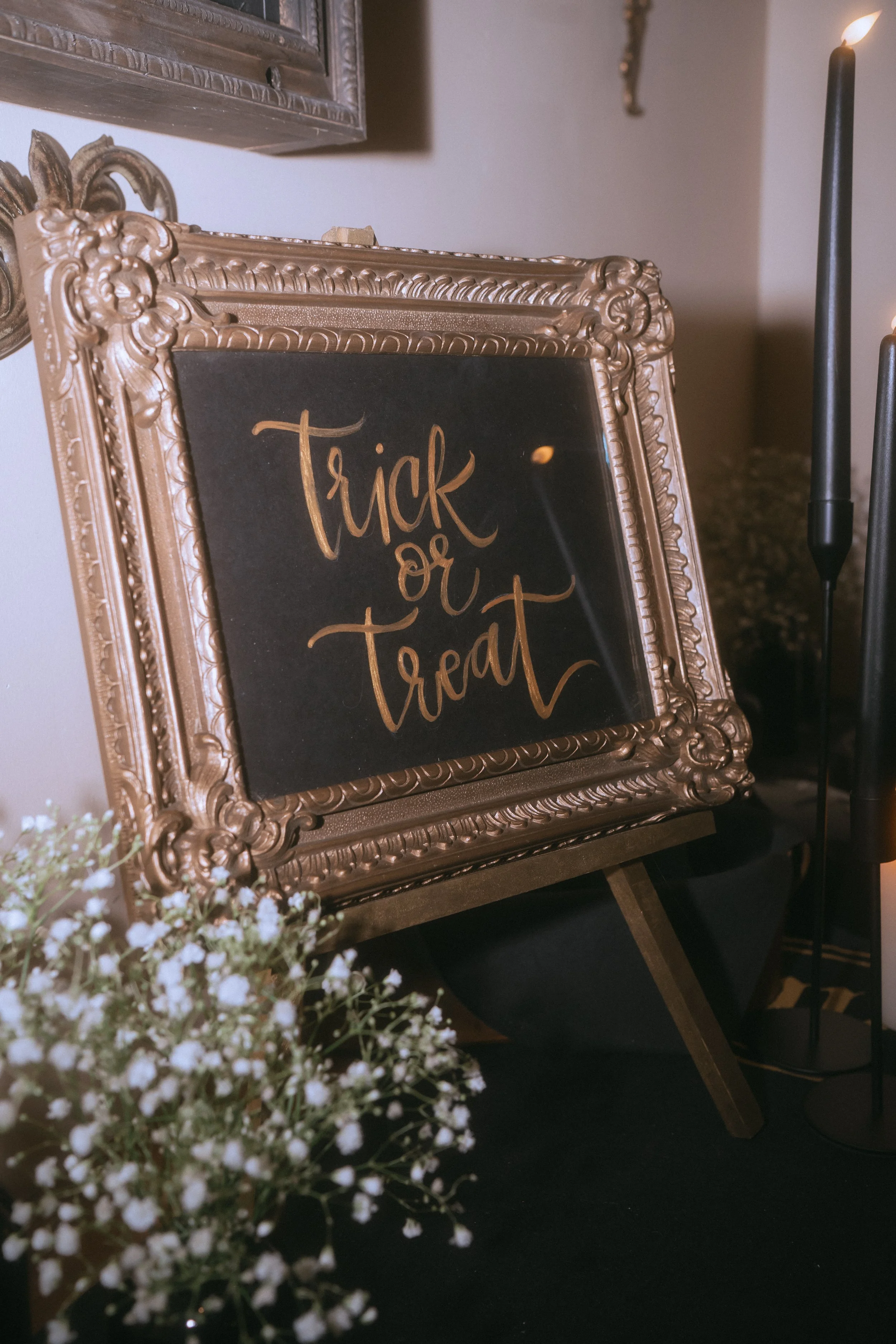 Framed black and gold “Trick or Treat” sign displayed as Halloween-inspired wedding decor with candles