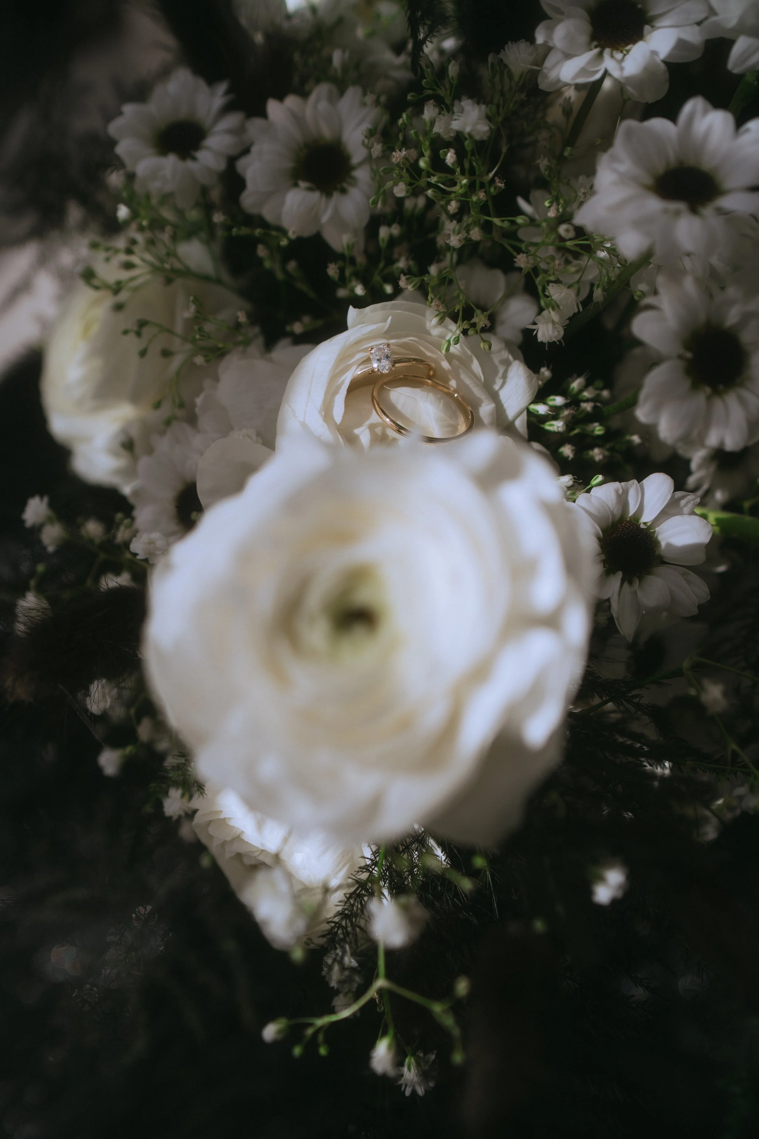 Close-up of wedding rings nestled in a white floral bouquet with soft, romantic lighting and delicate blooms