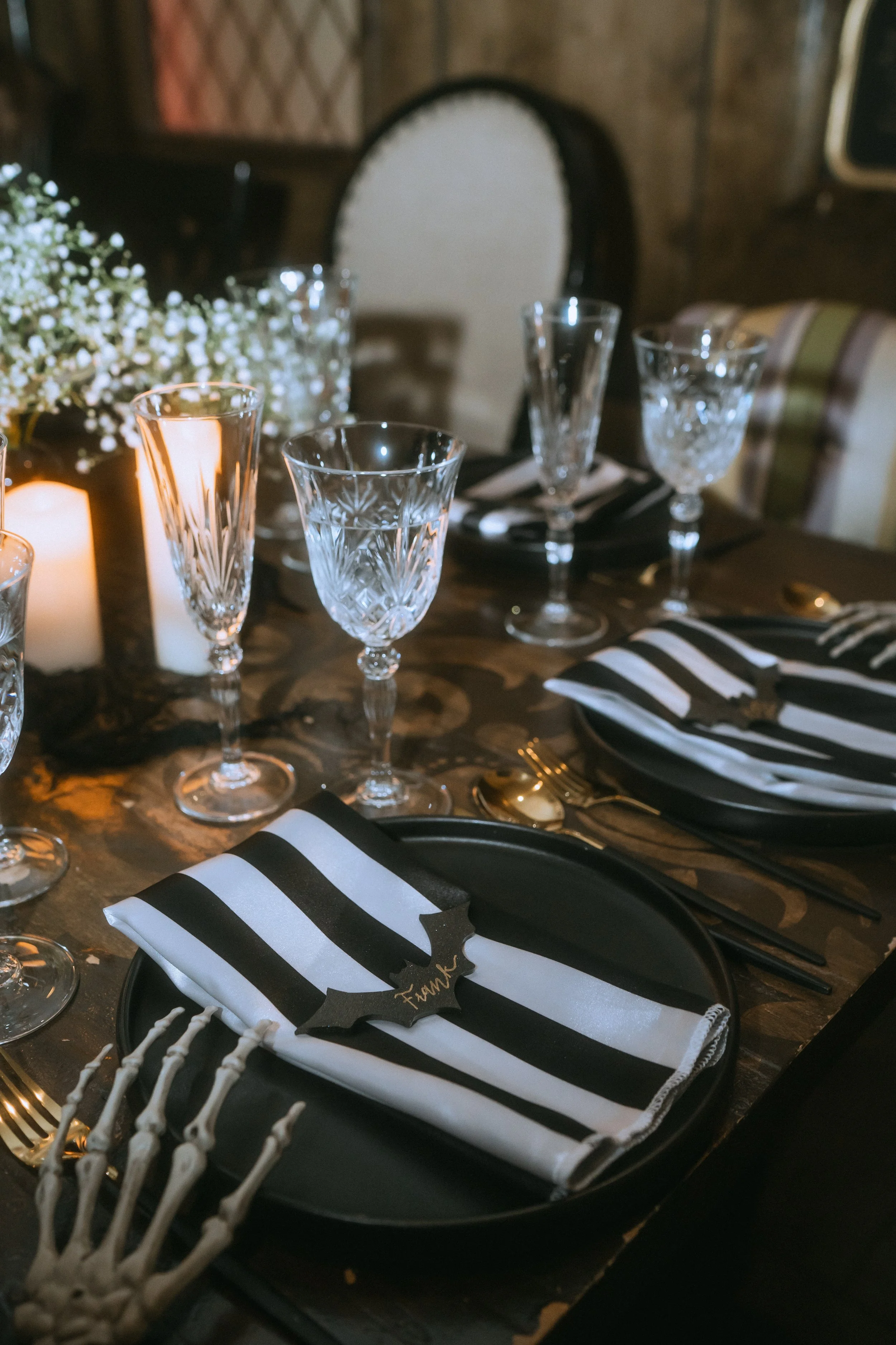 Moody non-traditional wedding tablescape with black plates, striped napkins, skeleton hand flatware, crystal glassware, and candlelight ambiance
