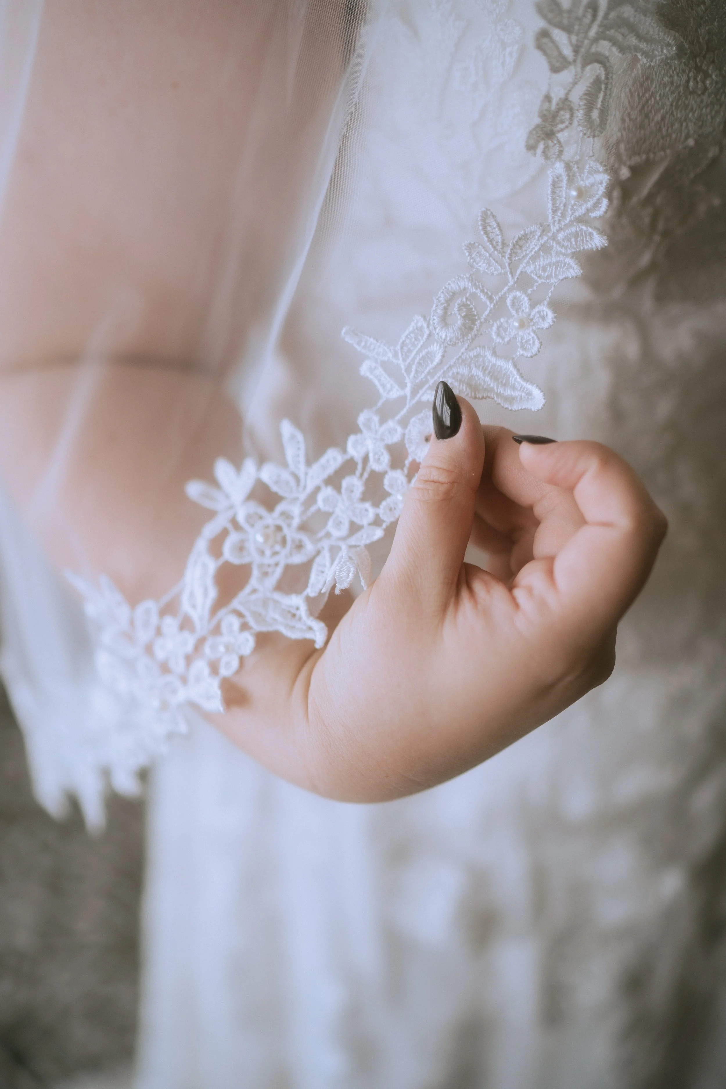 Close-up of a bride’s hand holding delicate lace sleeve detail on a wedding dress with soft natural light