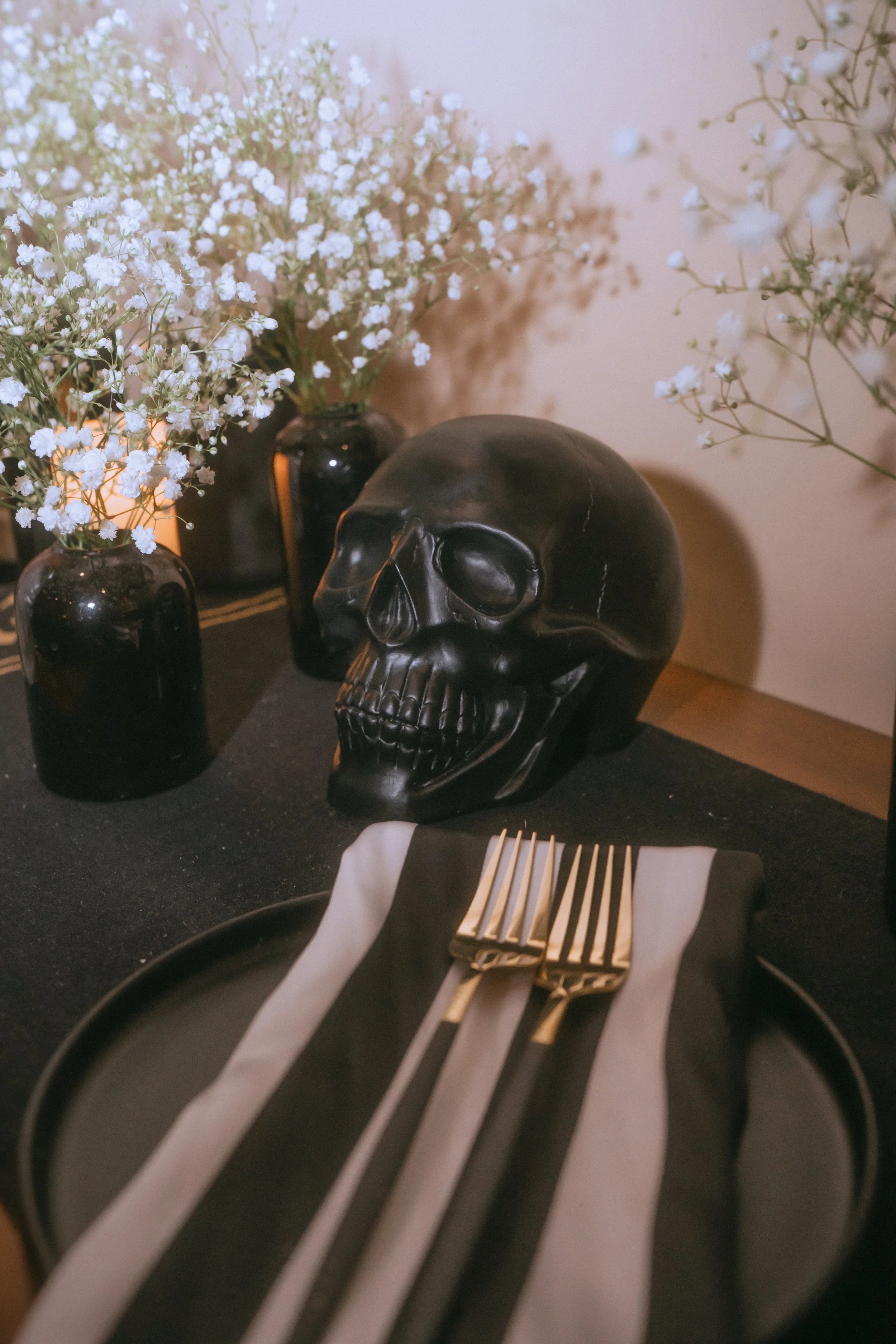 Black skull decor placed on a moody non-traditional wedding tablescape with striped napkins, gold flatware, and soft candlelight