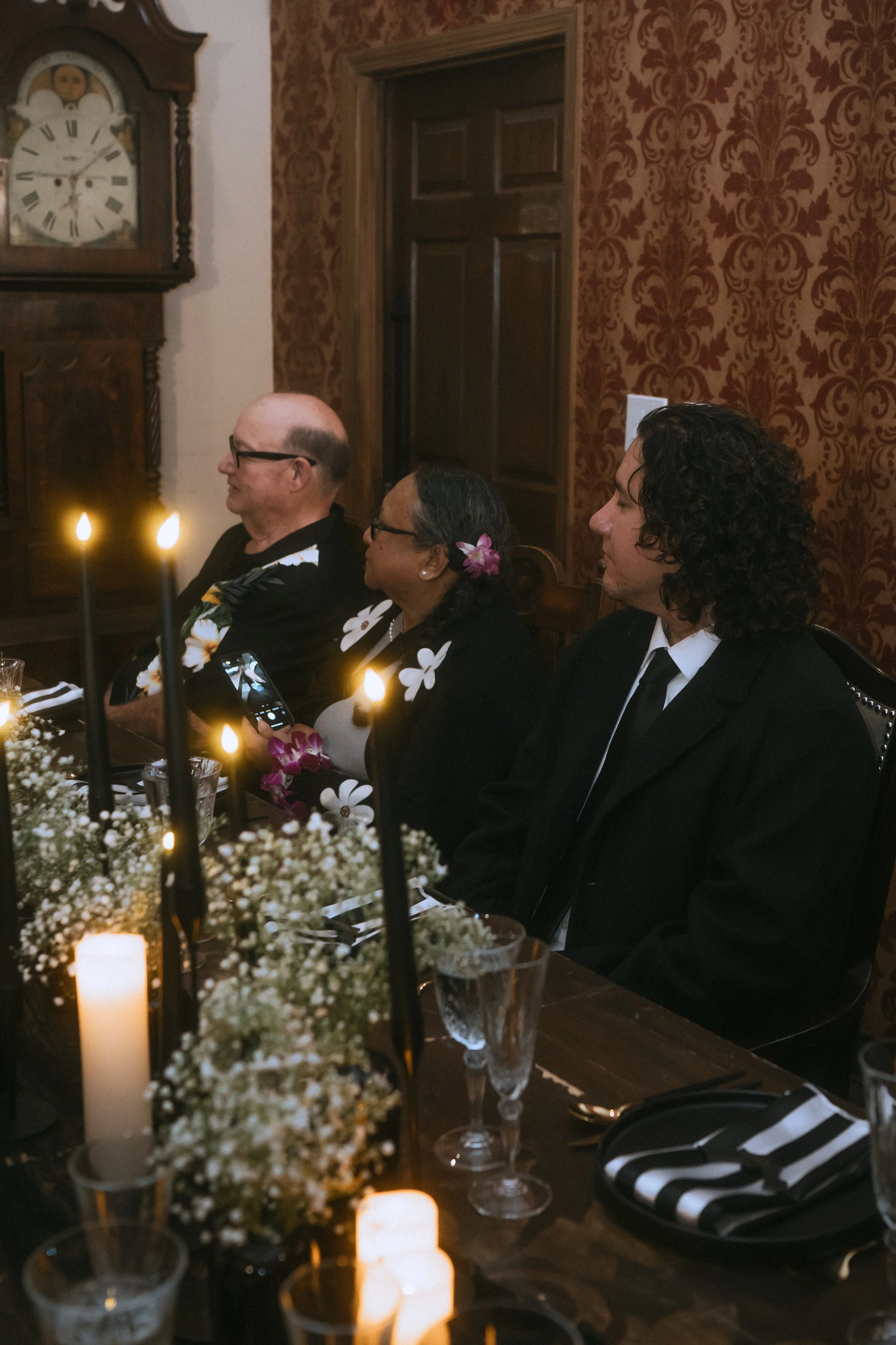 Wedding guests seated at a candlelit reception table with black taper candles and floral centerpieces