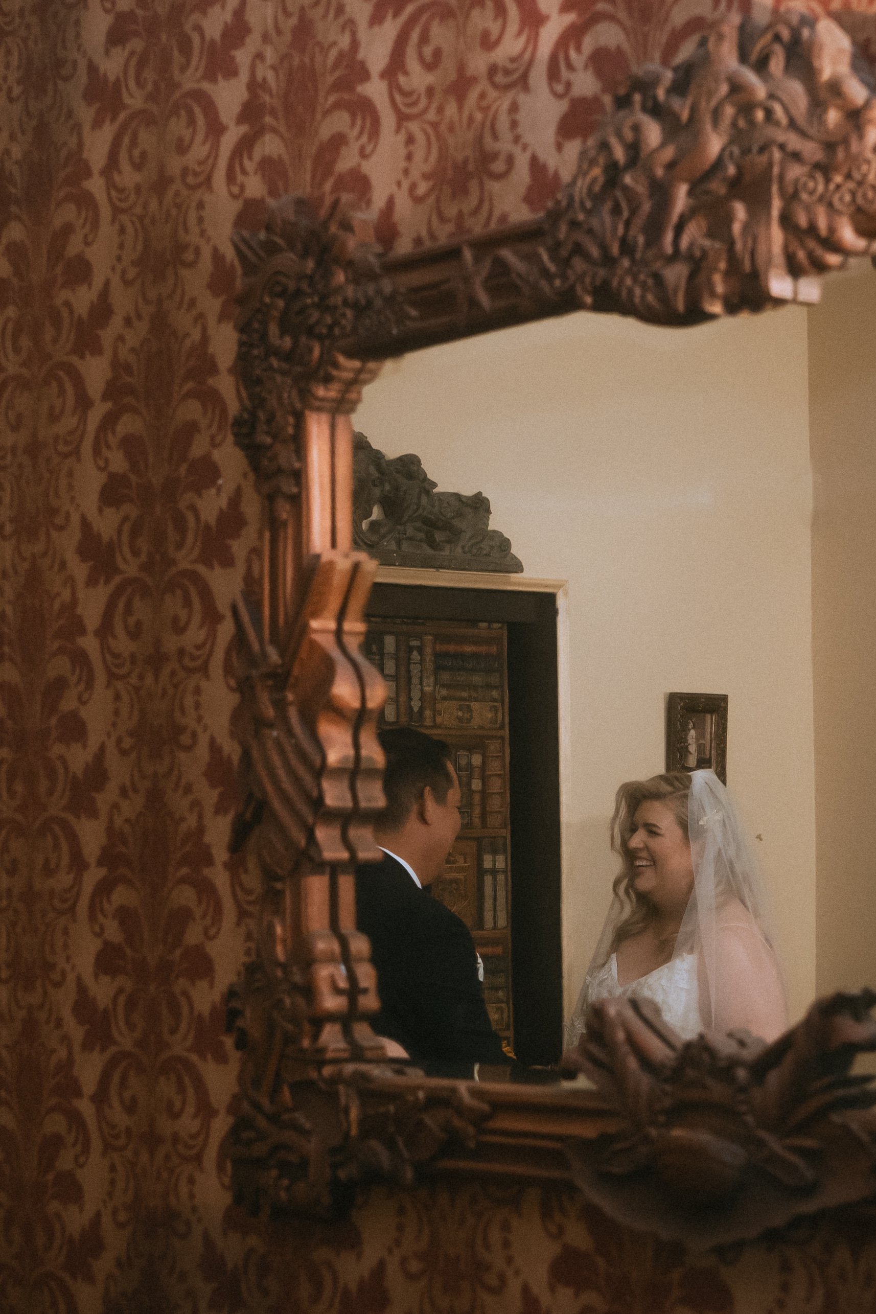 Bride and groom smiling at each other reflected in an ornate vintage mirror during an intimate wedding moment