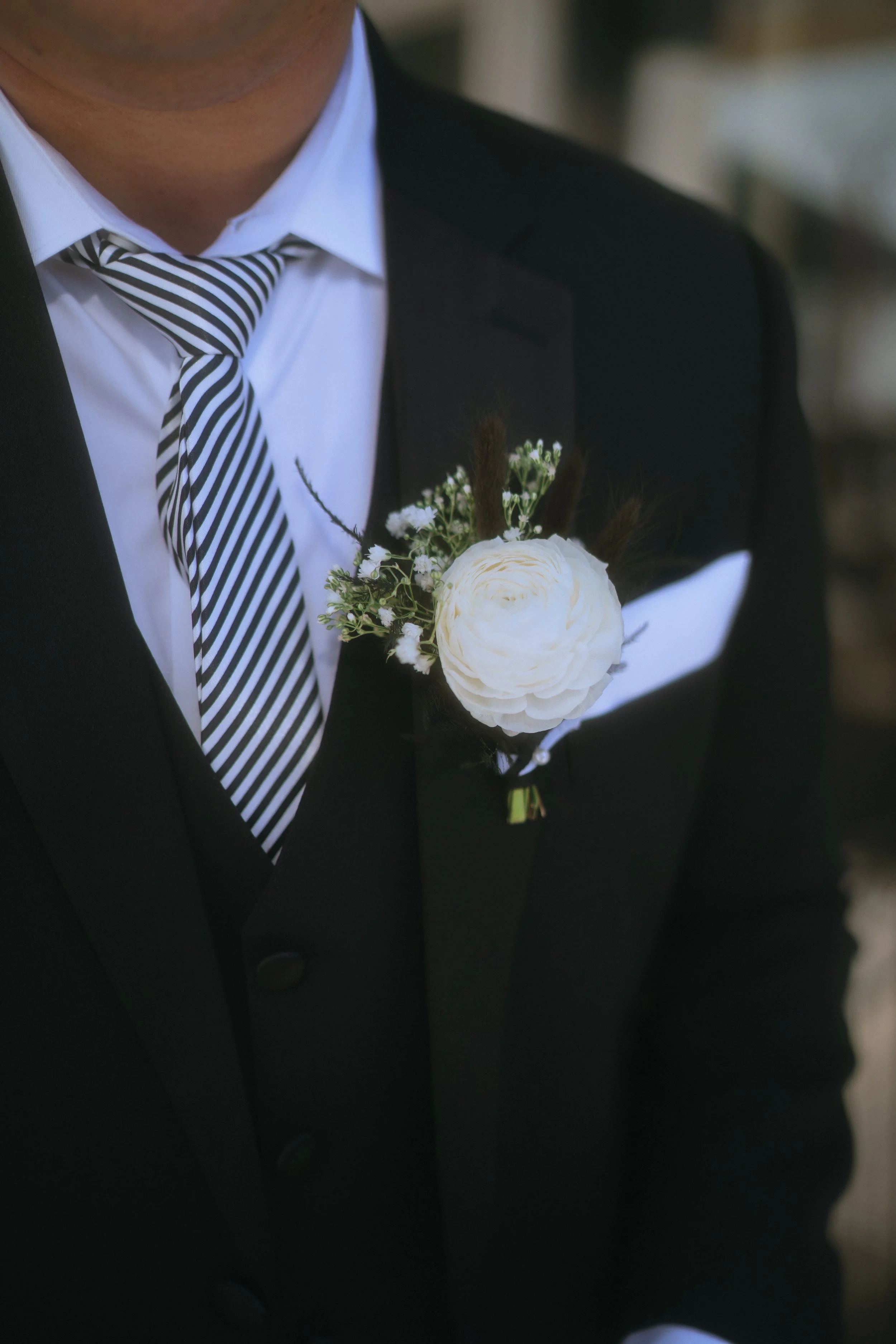 Close-up of groom in a black suit with a white floral boutonniere and striped tie