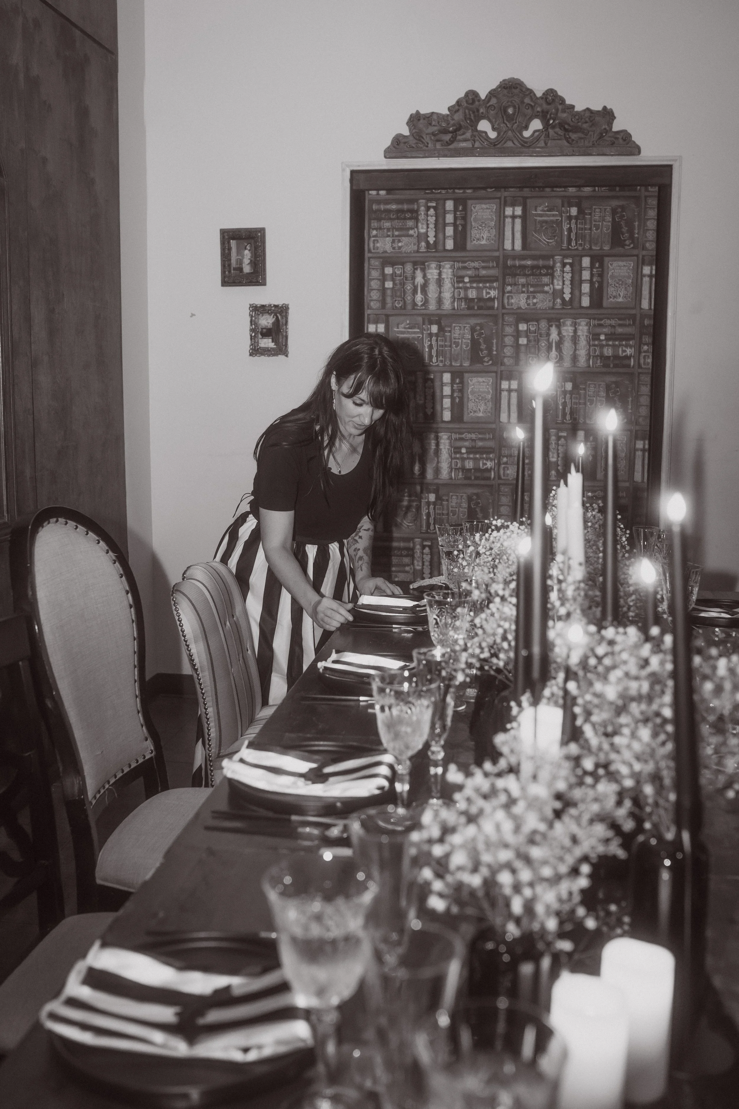 Person adjusting place settings on a candlelit wedding table with black and white decor and floral arrangements