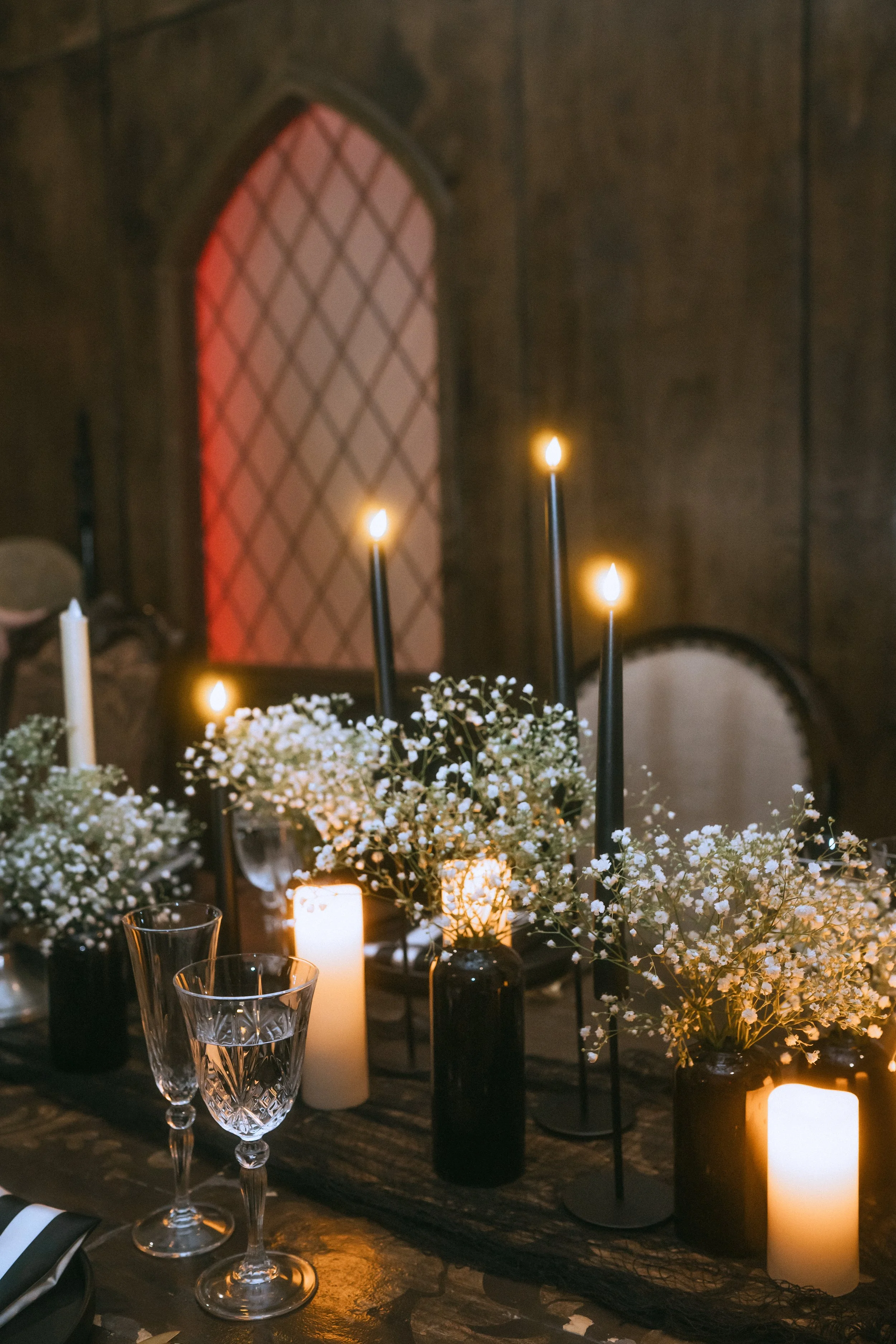 Moody wedding table with black taper candles, baby’s breath centerpieces, and a vintage window backdrop