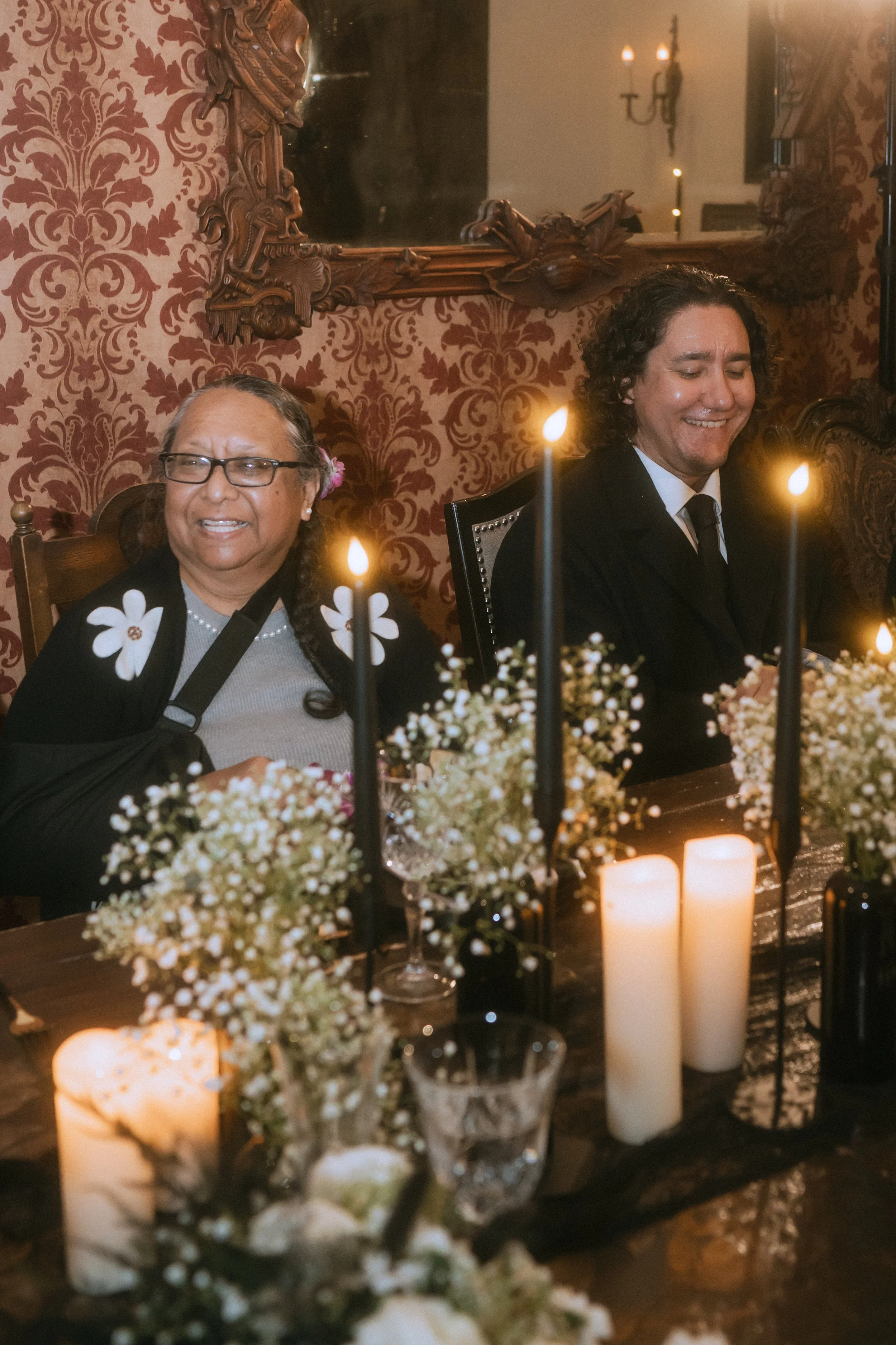 Family members seated at a candlelit wedding reception table with black taper candles and floral decor