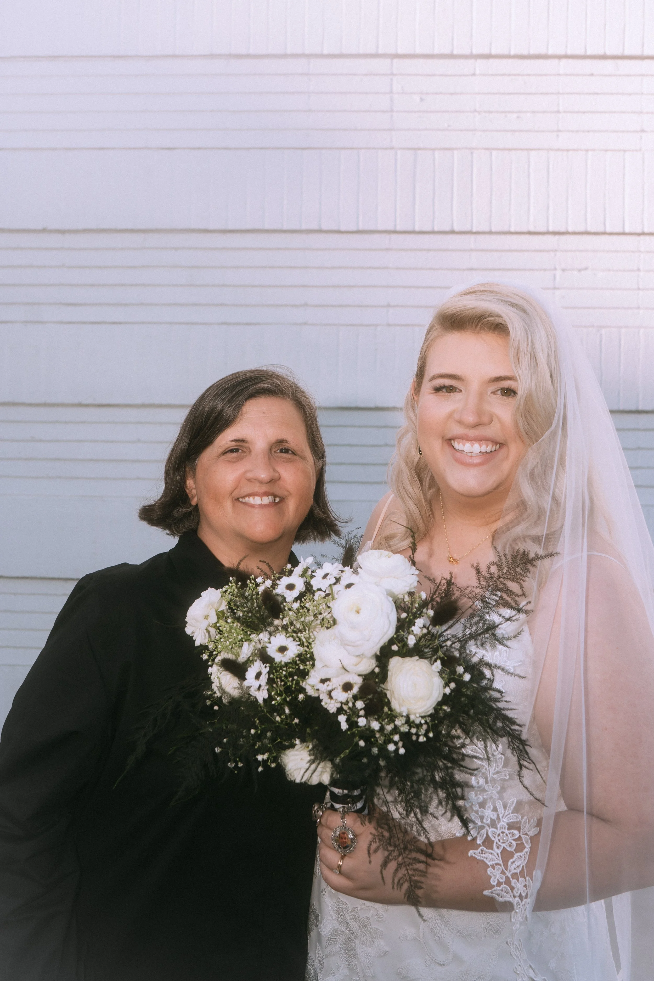 Bride smiling with an older woman, holding a white floral bouquet during a wedding portrait