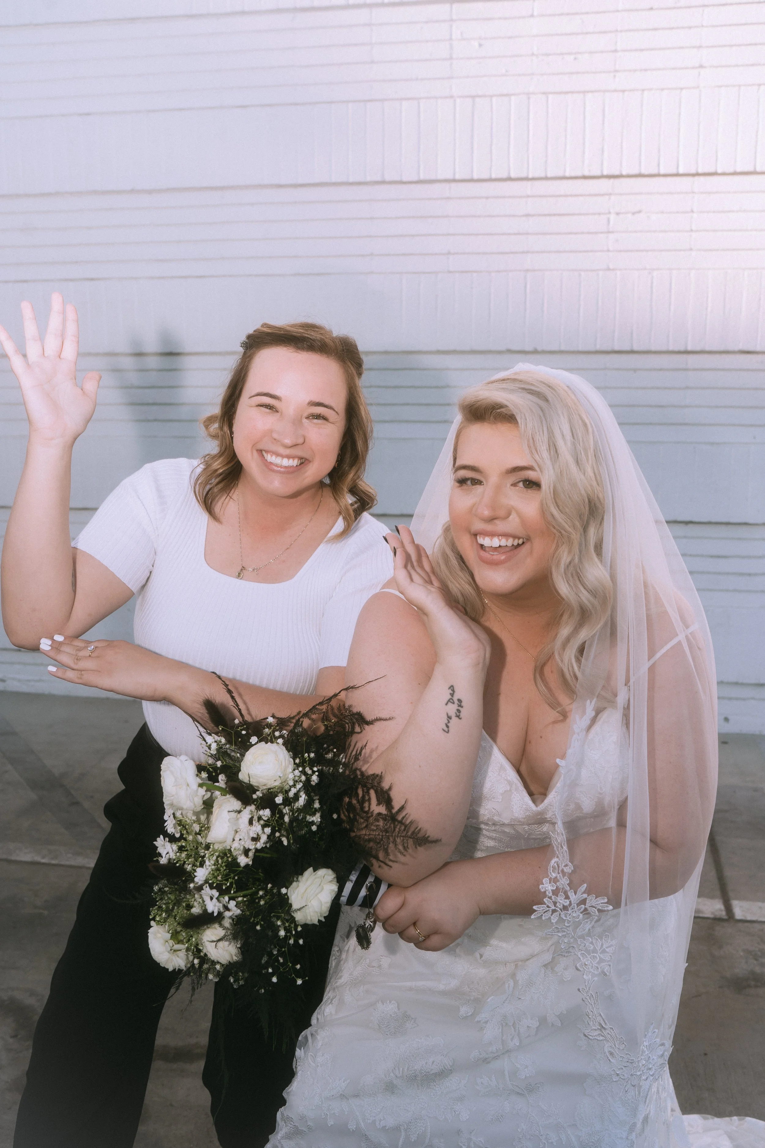 Bride and bridesmaid posing playfully together holding a bouquet during a wedding portrait