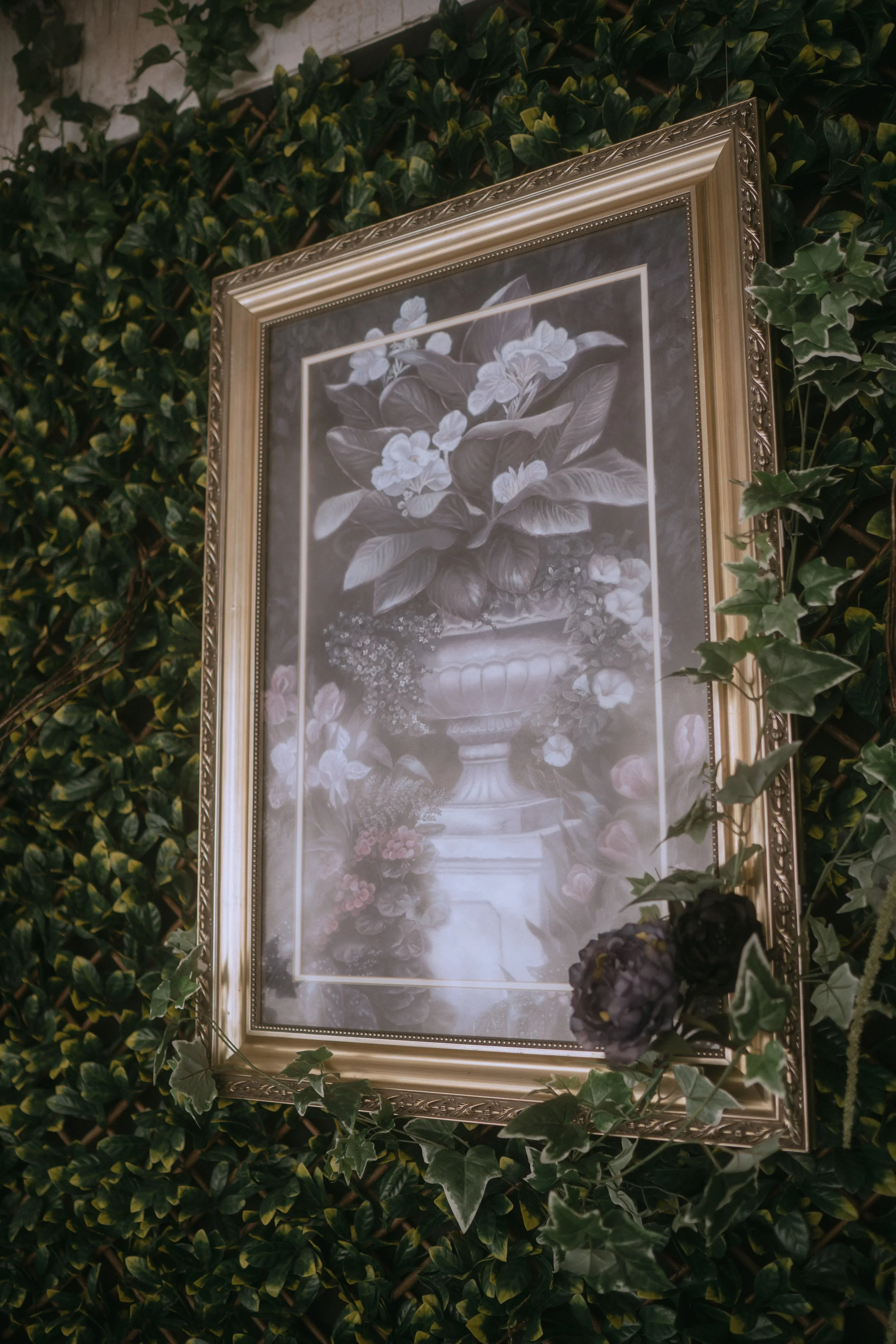 Framed vintage floral artwork displayed against a lush greenery wall as romantic wedding decor