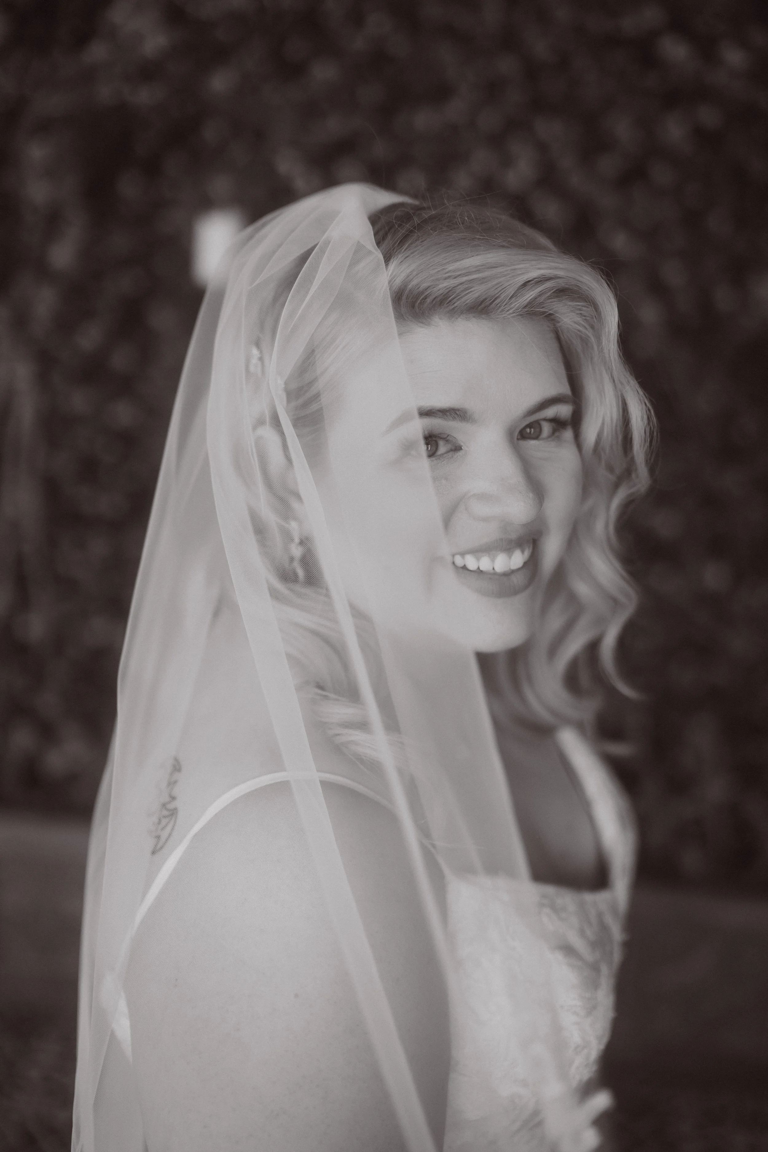 Black and white close-up portrait of bride smiling through veil during wedding day