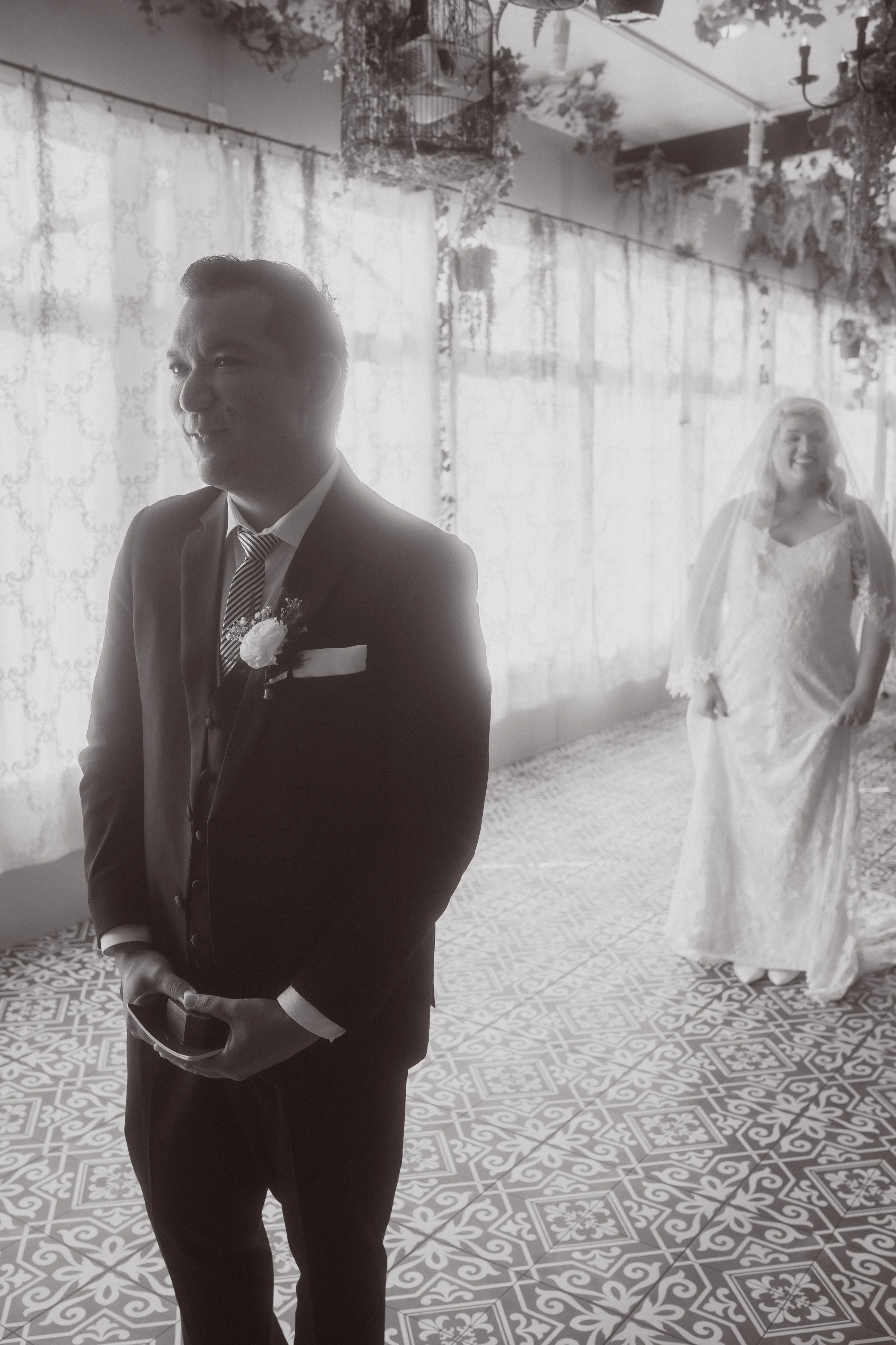 Bride walking up behind groom for first look inside wedding venue with patterned tile floor and soft light
