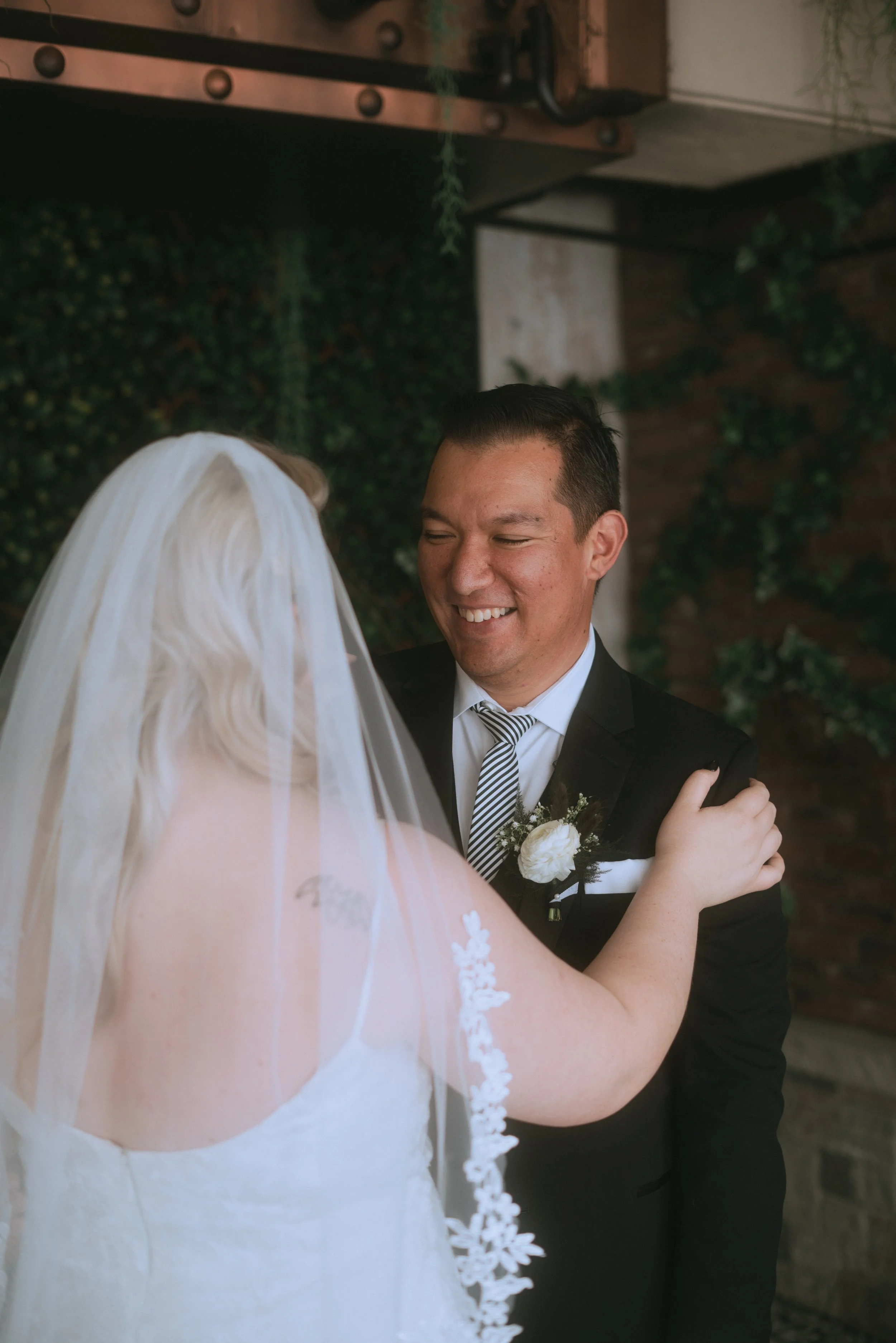 Groom smiling during first look as he sees bride in wedding dress with veil in an intimate moment
