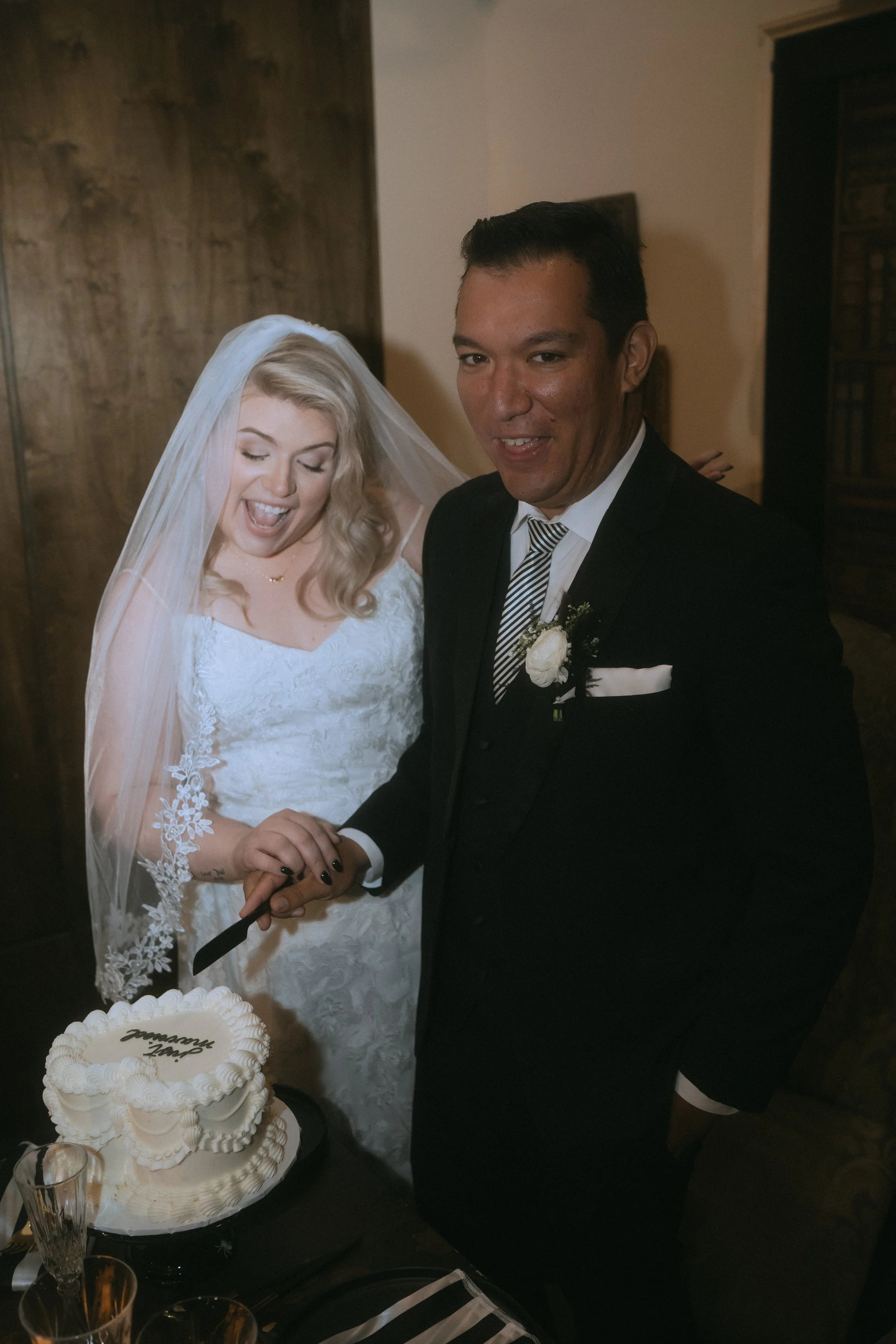 Bride and groom smiling while cutting wedding cake together during reception
