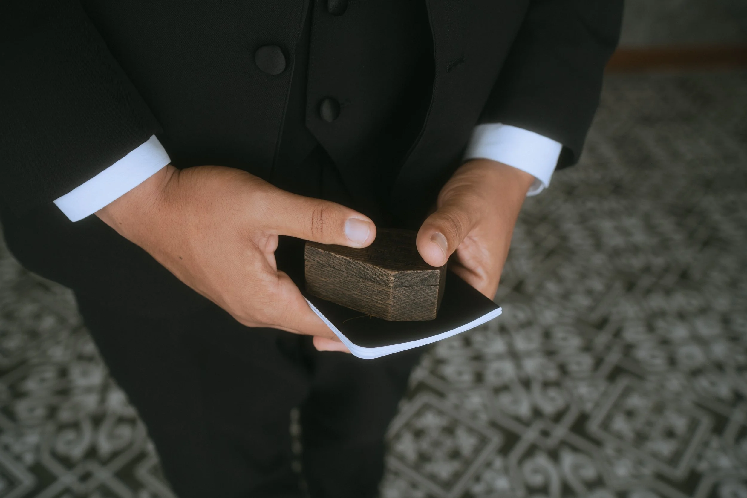 Close-up of groom’s hands holding wooden ring box and small book during wedding ceremony