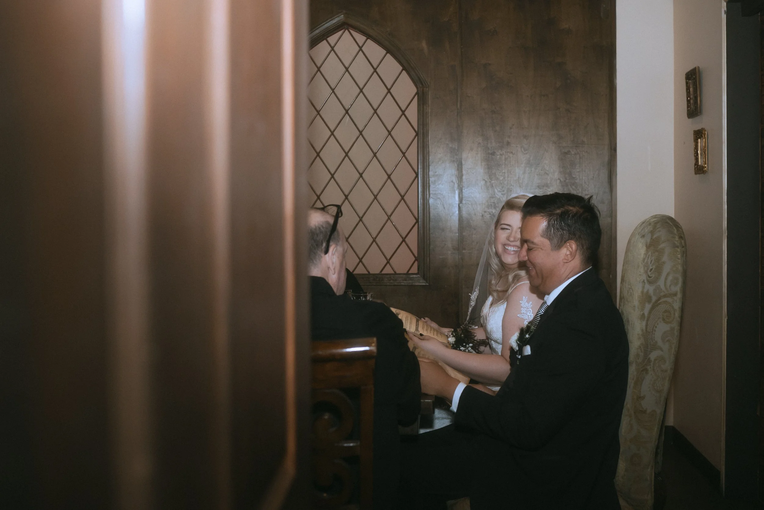 Bride and groom seated together smiling and laughing during intimate wedding ceremony with officiant nearby