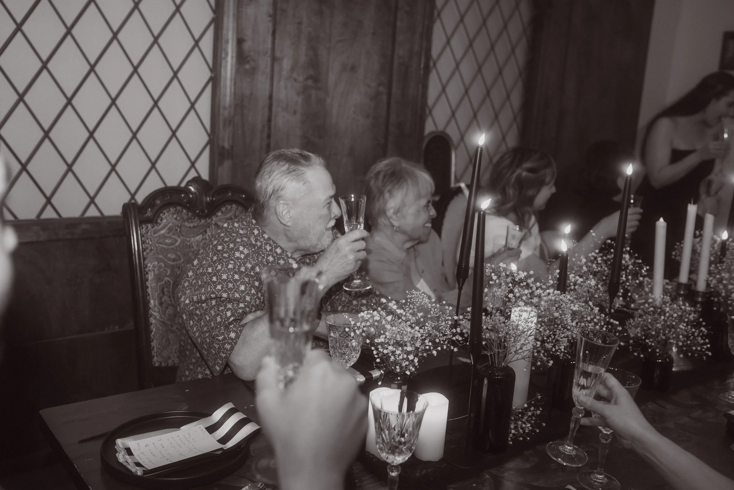 Wedding guests raising glasses for a toast at candlelit reception table with floral arrangements