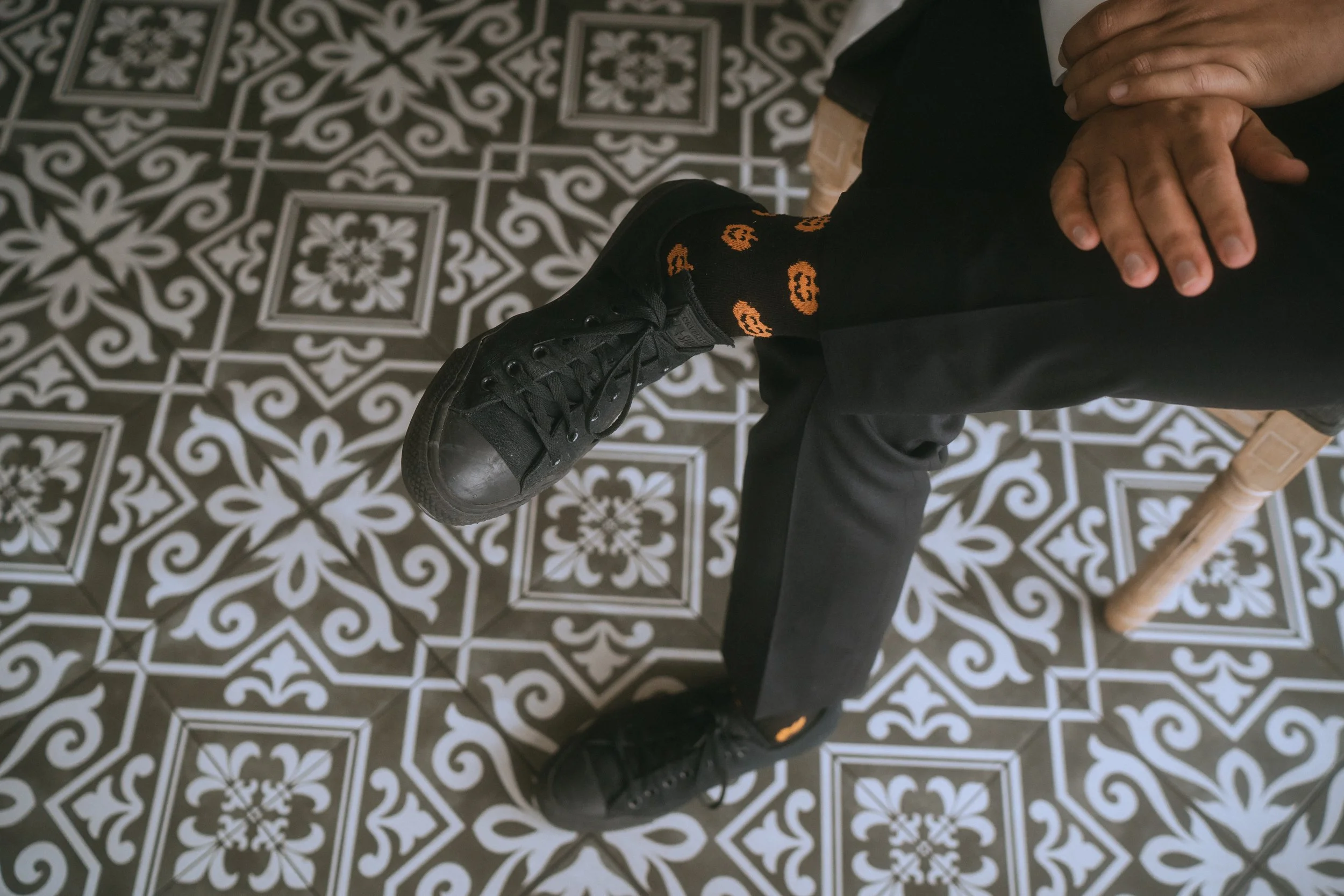Close-up of groom sitting with black sneakers and patterned socks on decorative tile floor