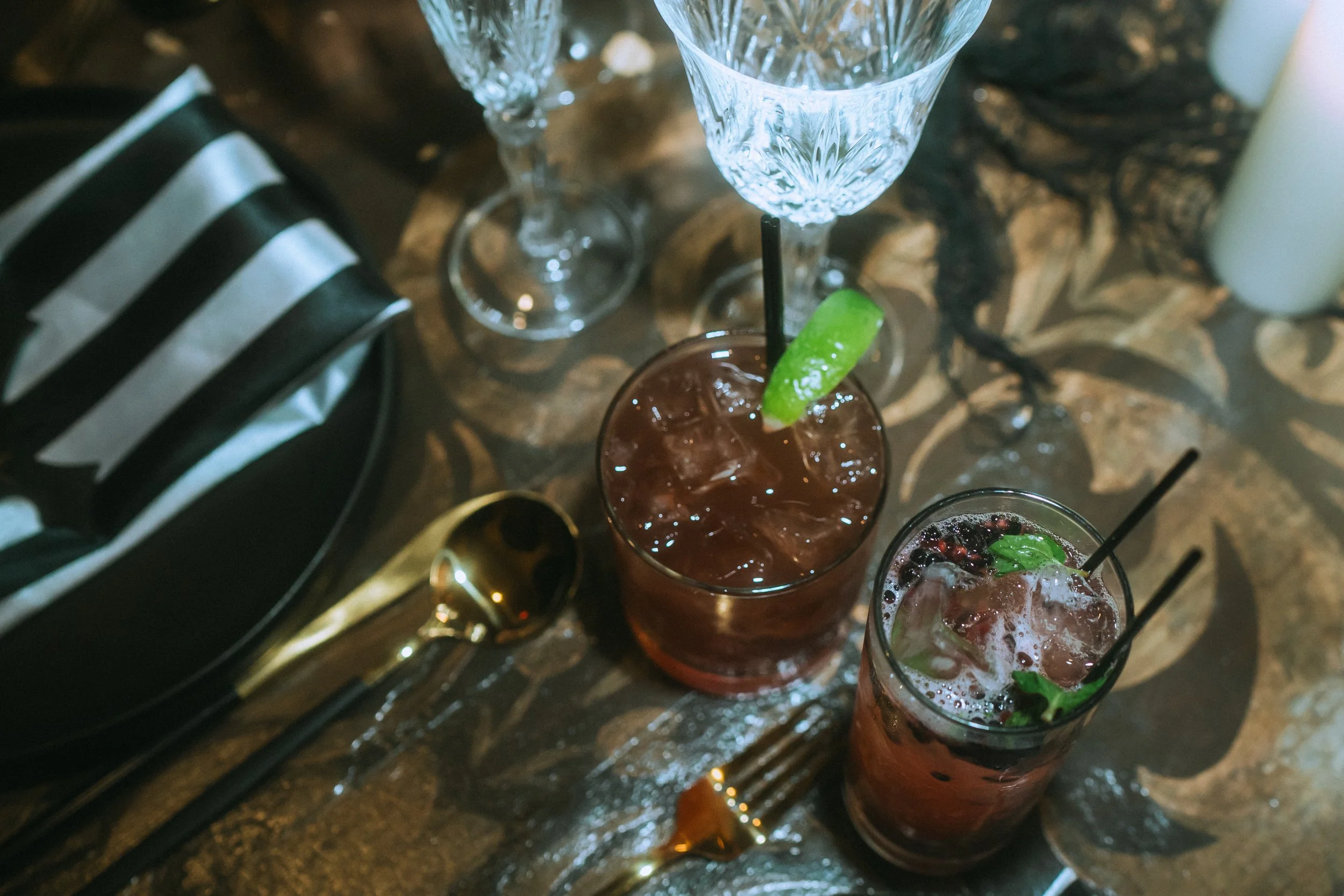 Wedding cocktails with lime garnish and berries on reception table with crystal glassware and striped napkin
