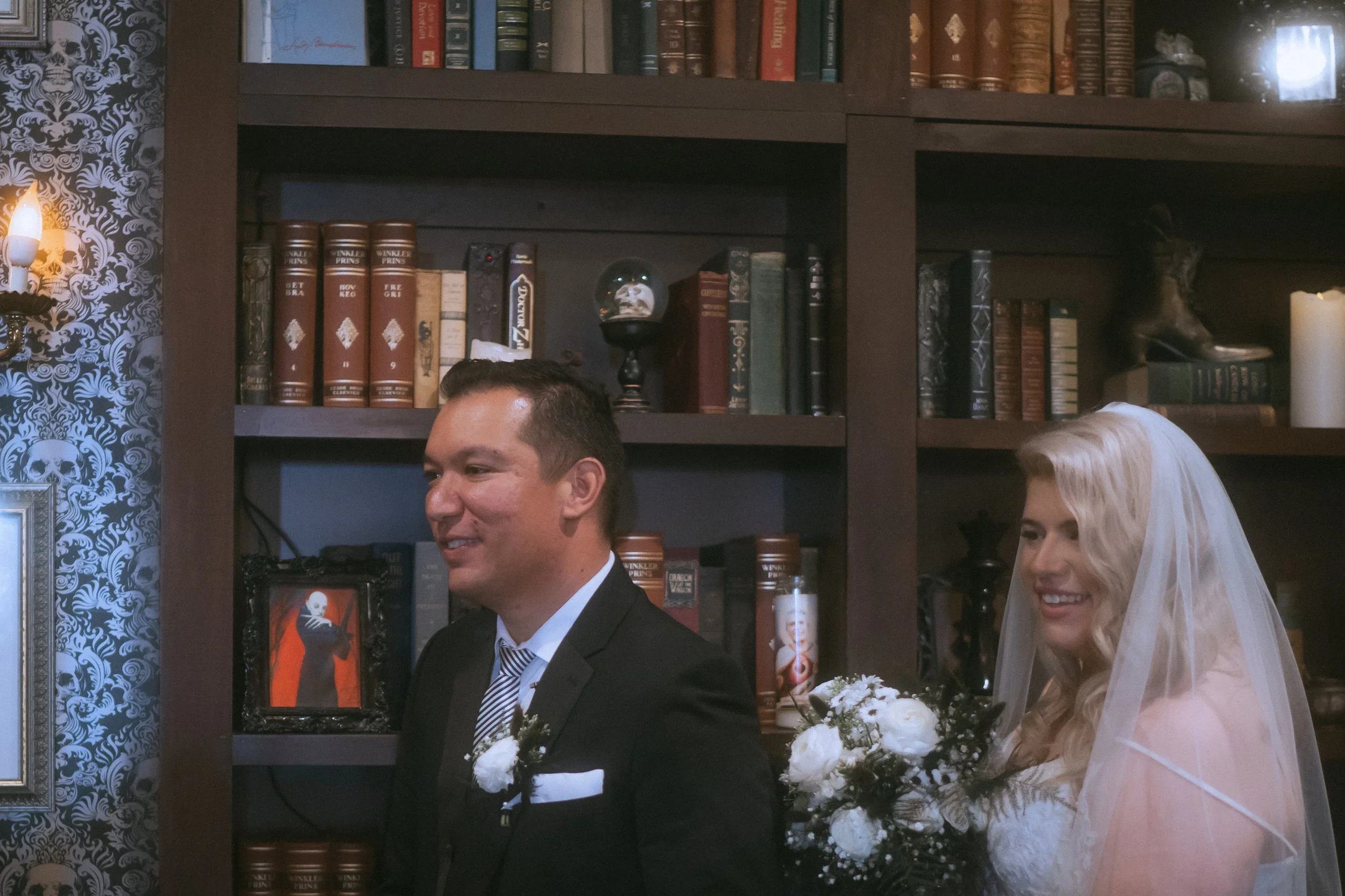 Bride and groom smiling during intimate ceremony entrance with candlelit bookshelf backdrop