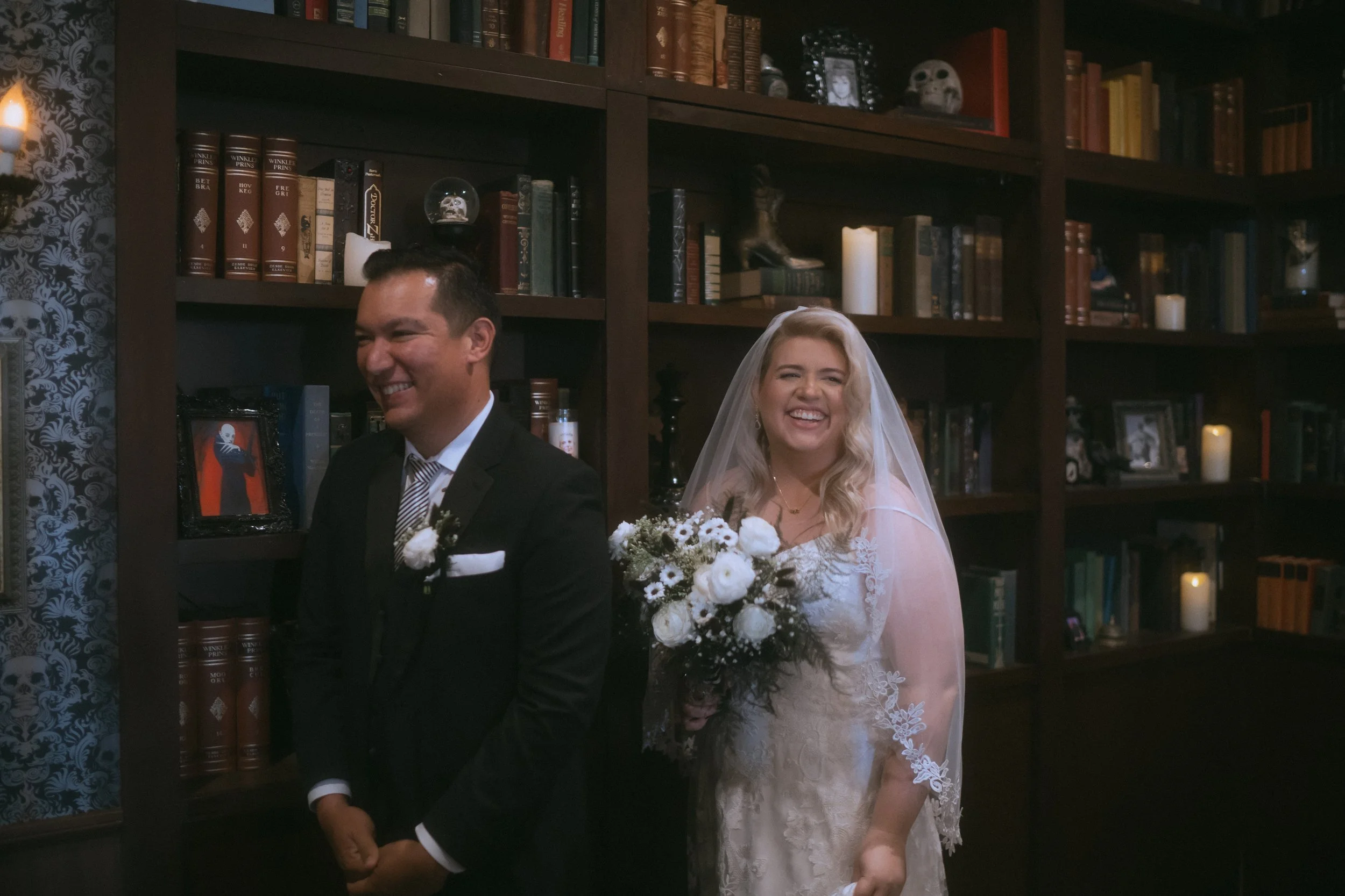 Bride and groom standing together in front of dark bookshelf backdrop with candles and vintage decor
