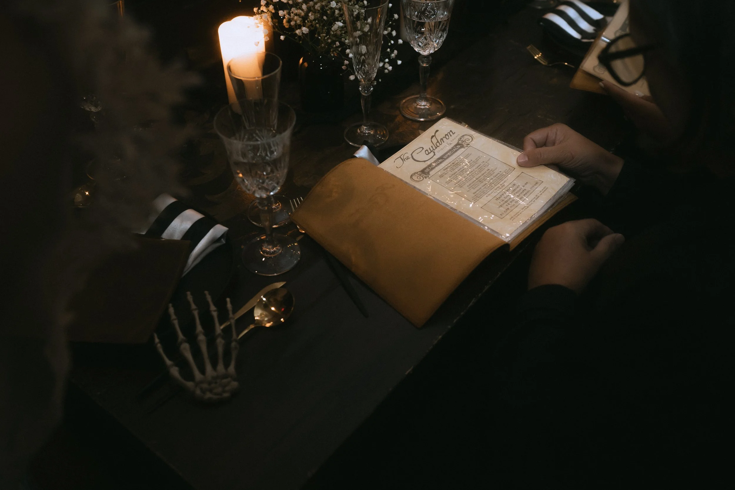 Close-up of wedding reception table with candlelight, glassware, striped napkin, and guest holding printed menu