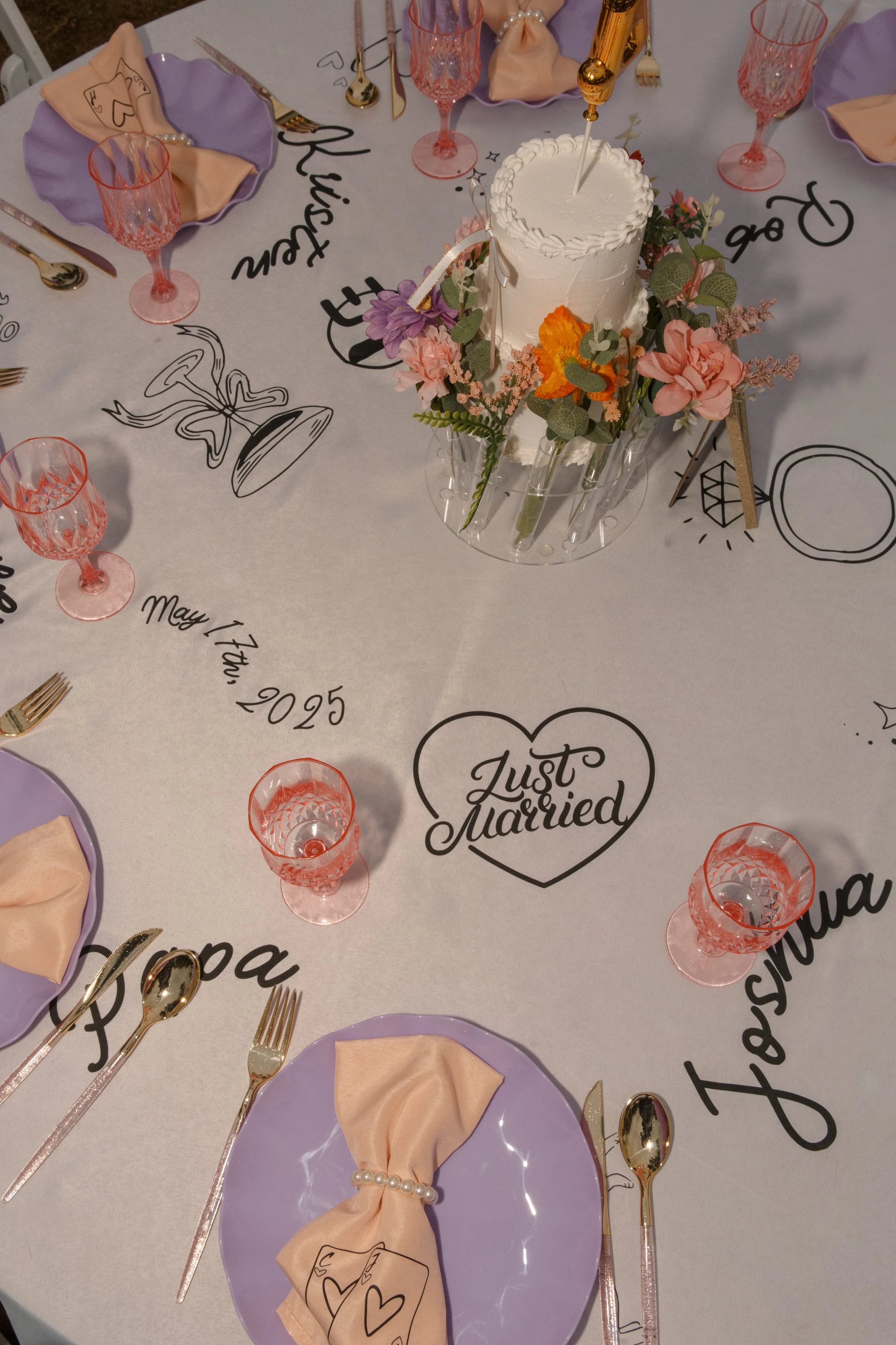 Overhead view of playful kitschy wedding tablescape with lavender plates, custom doodle table runner, and colorful centerpiece