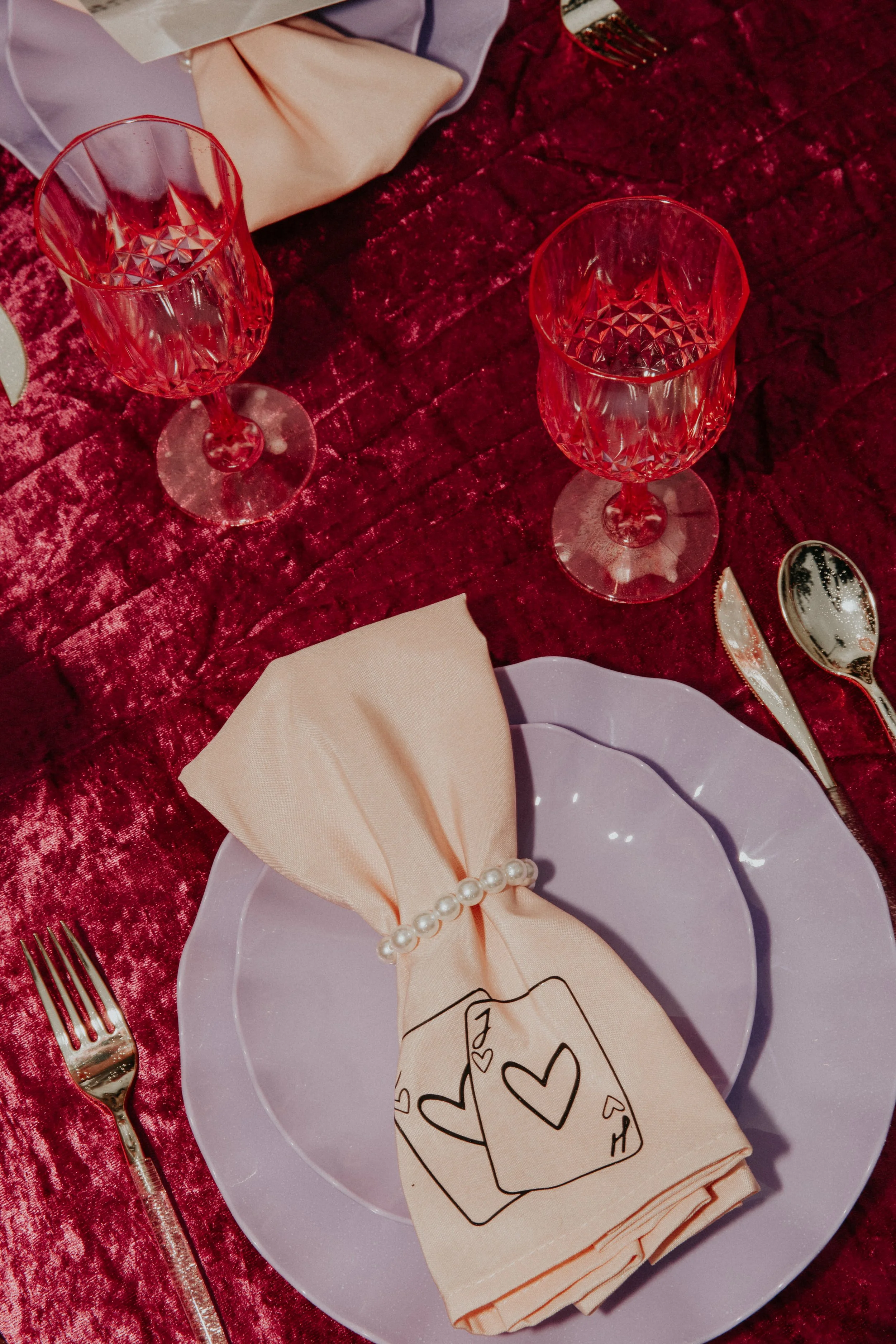 Bold colorful wedding table setting with velvet raspberry linens, lavender plates, gold flatware, and illustrated napkin detail