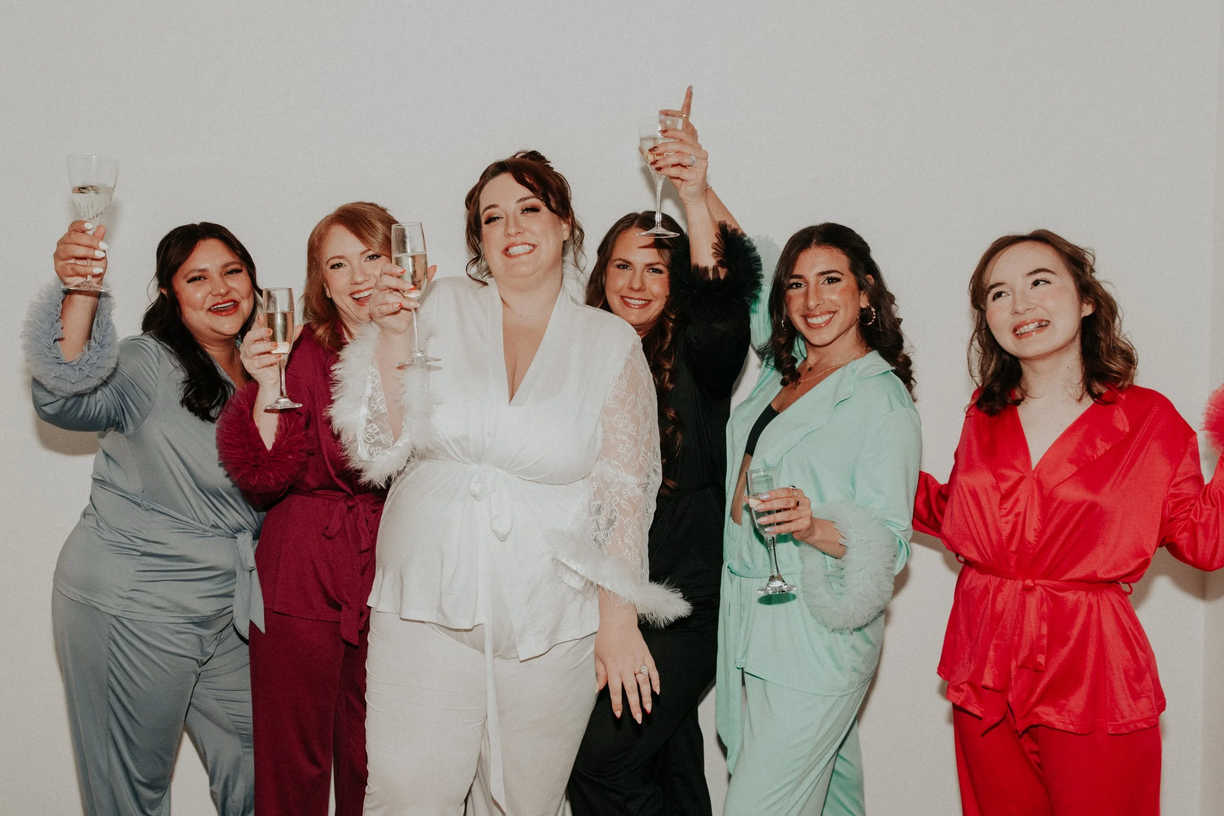 Bride and bridesmaids in colorful pajamas toasting champagne before wedding