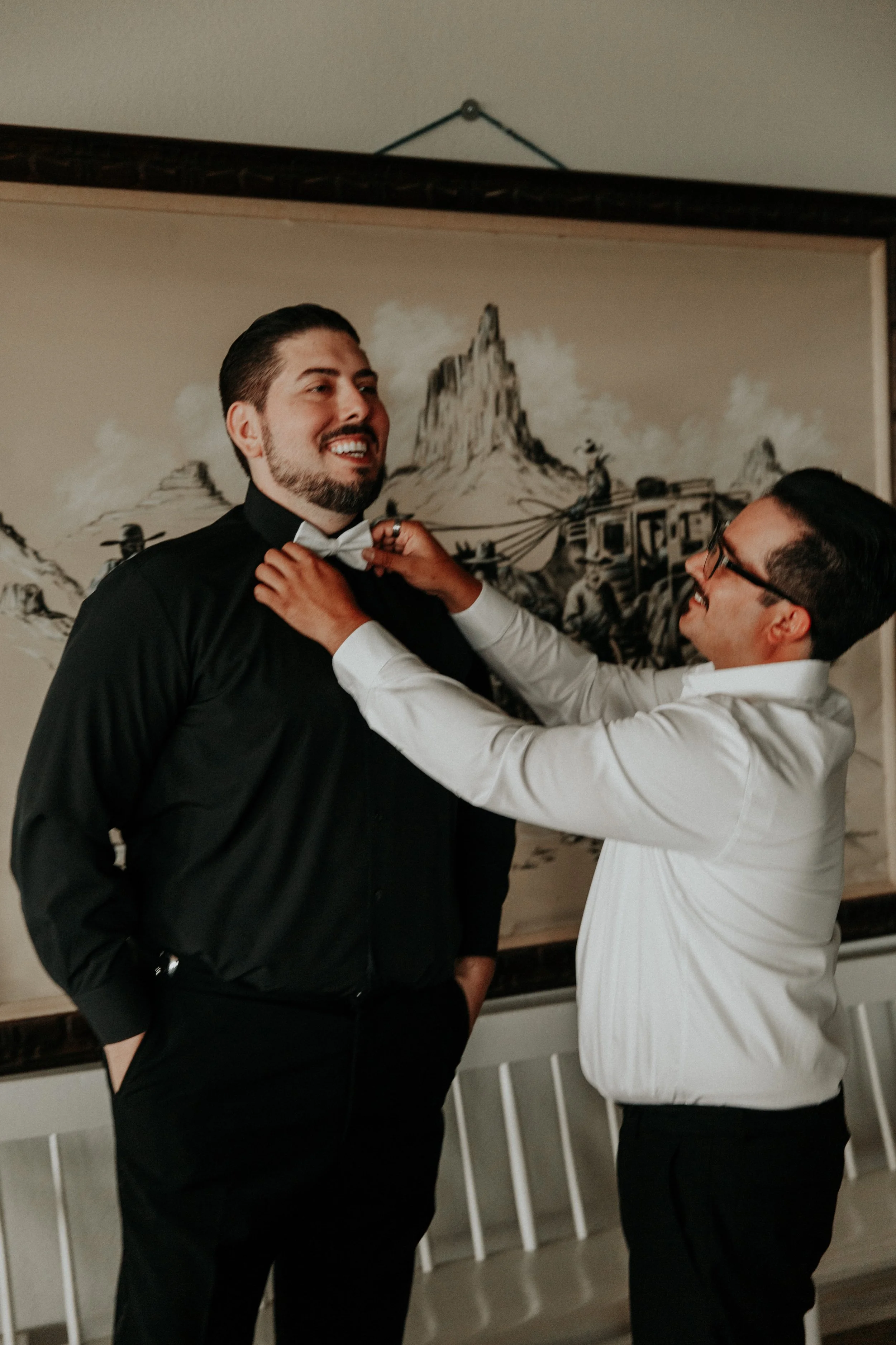 Groomsman helping groom straighten bowtie before wedding ceremony