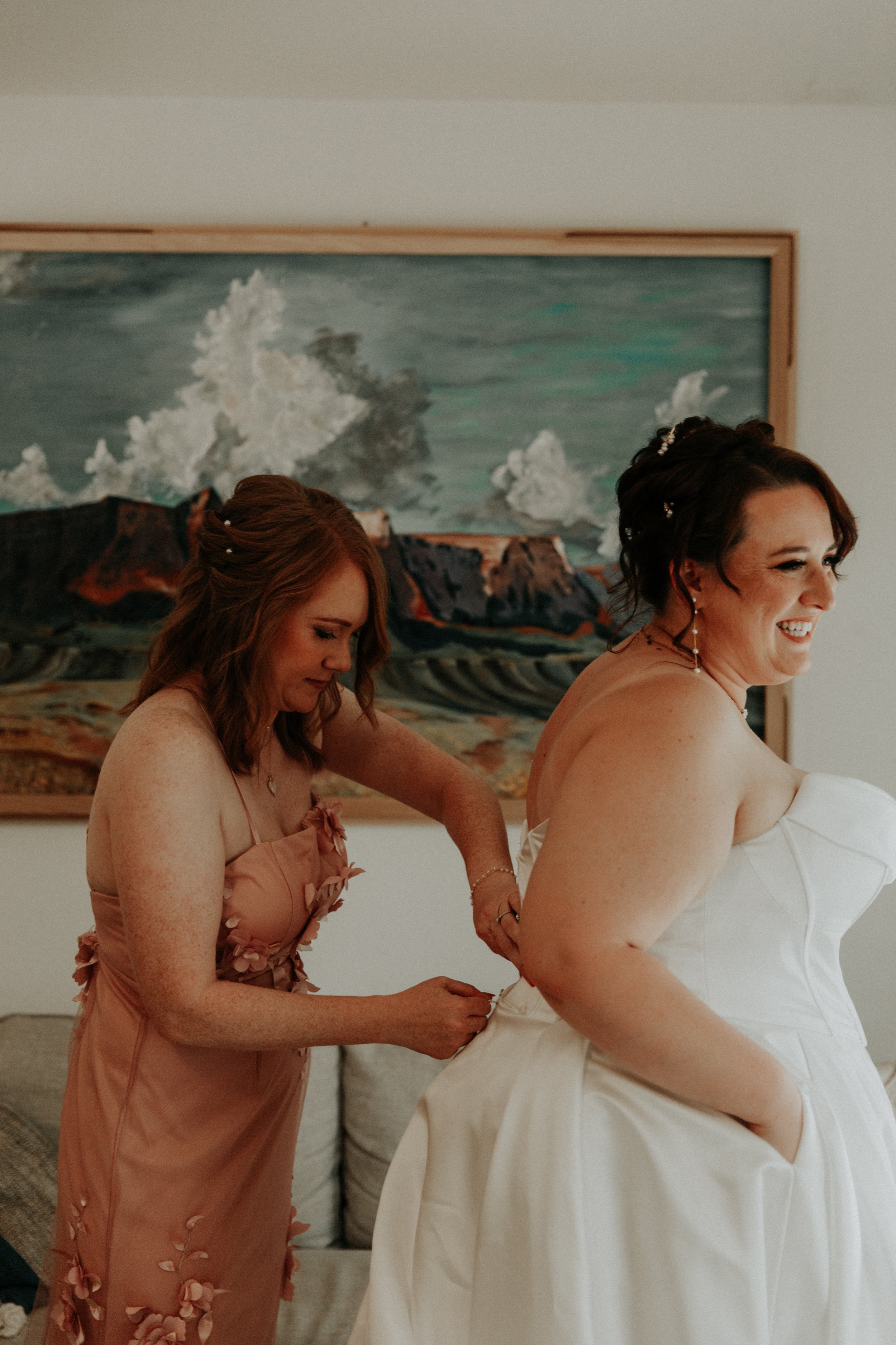 Bridesmaid fastening bride’s wedding dress during getting ready moments