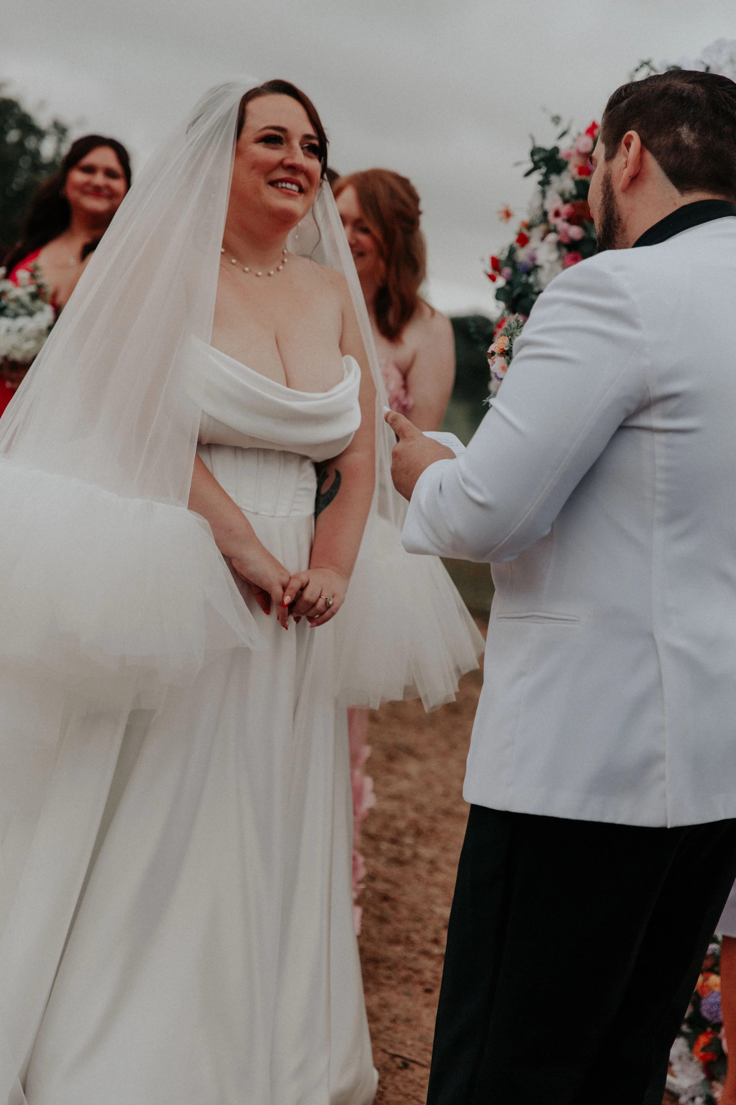 Bride smiling while groom reads vows during intimate outdoor wedding ceremony