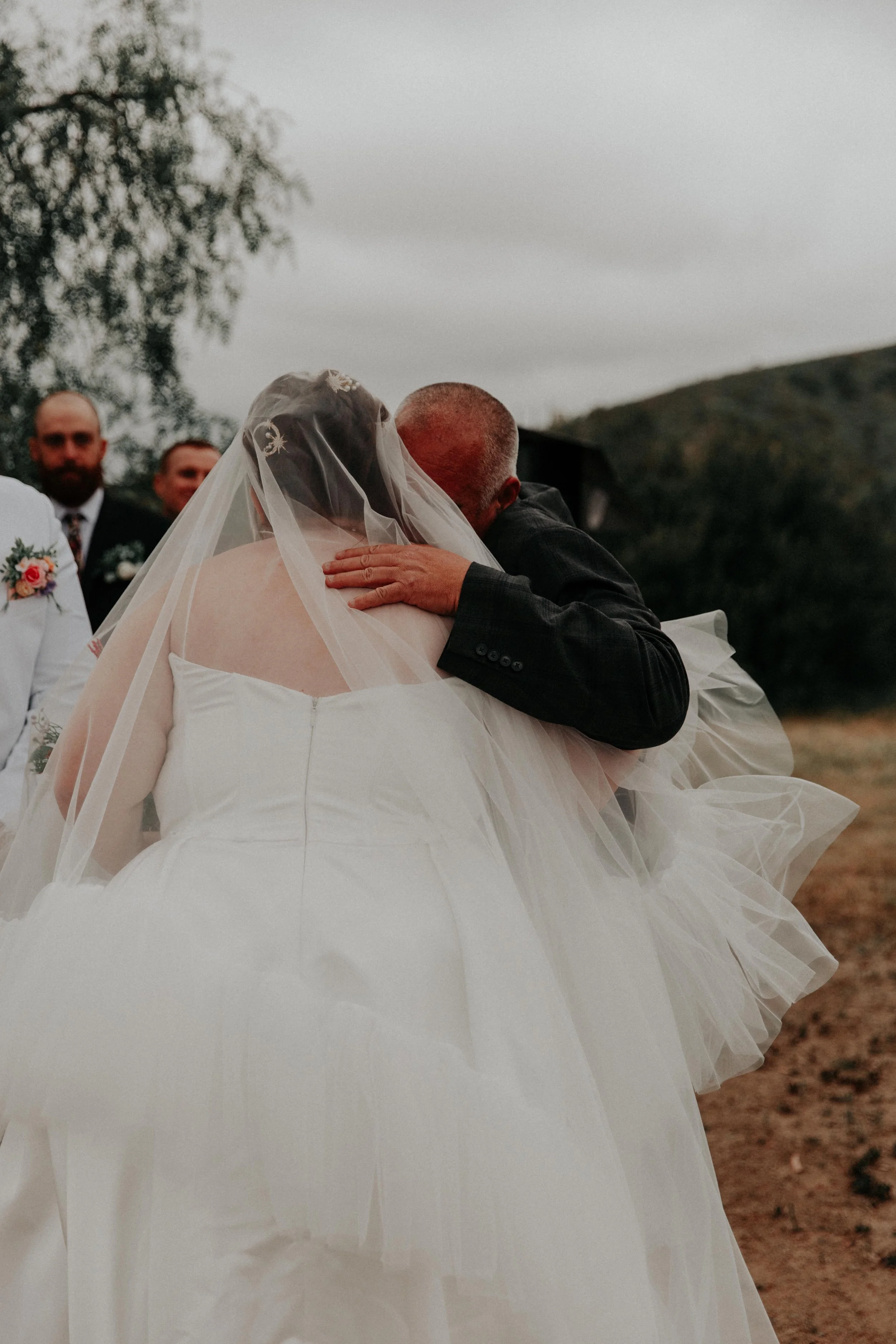 Emotional father hugging bride during outdoor wedding ceremony