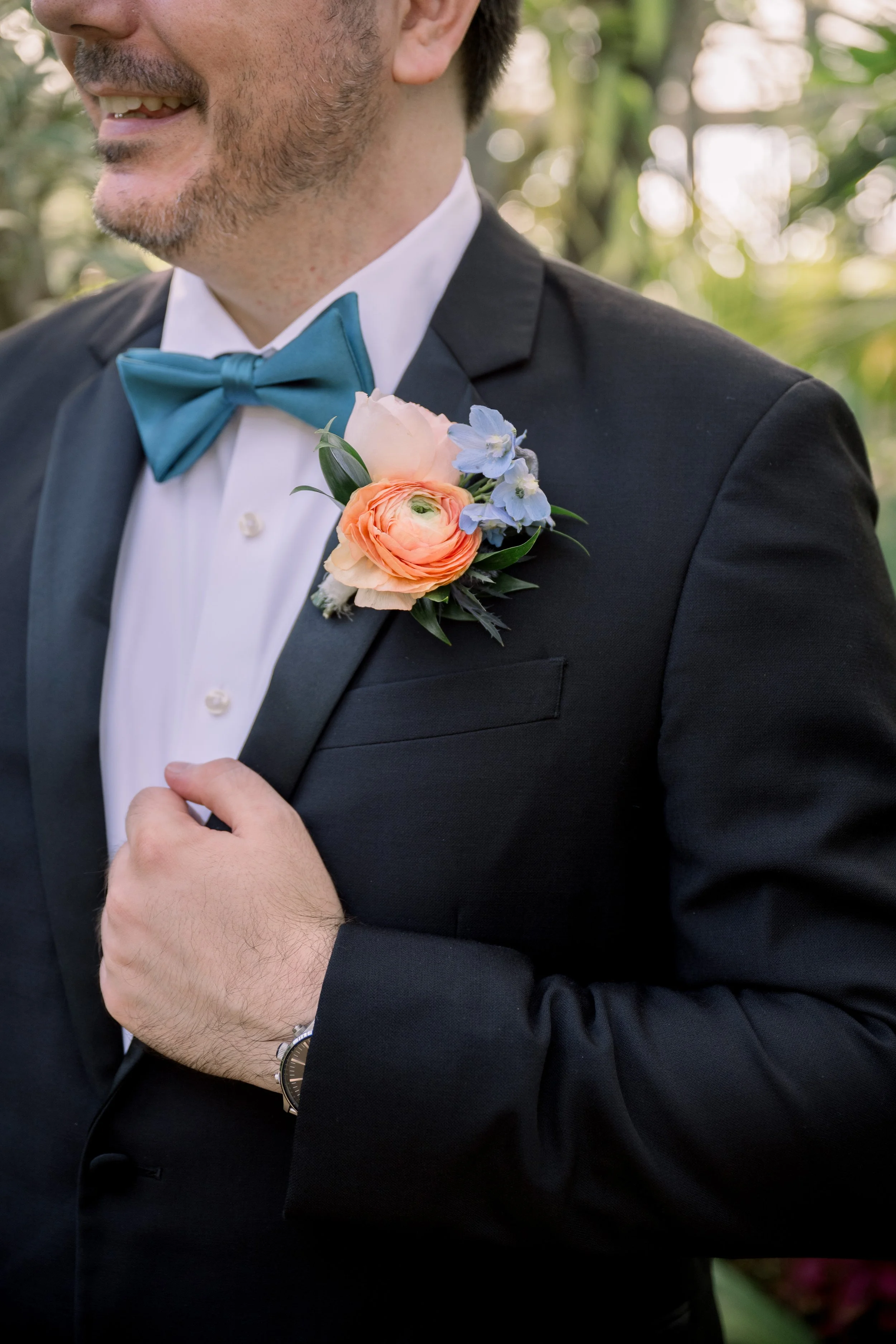 Close-up portrait of the groom’s floral boutonniere with a blue bow tie and black tuxedo