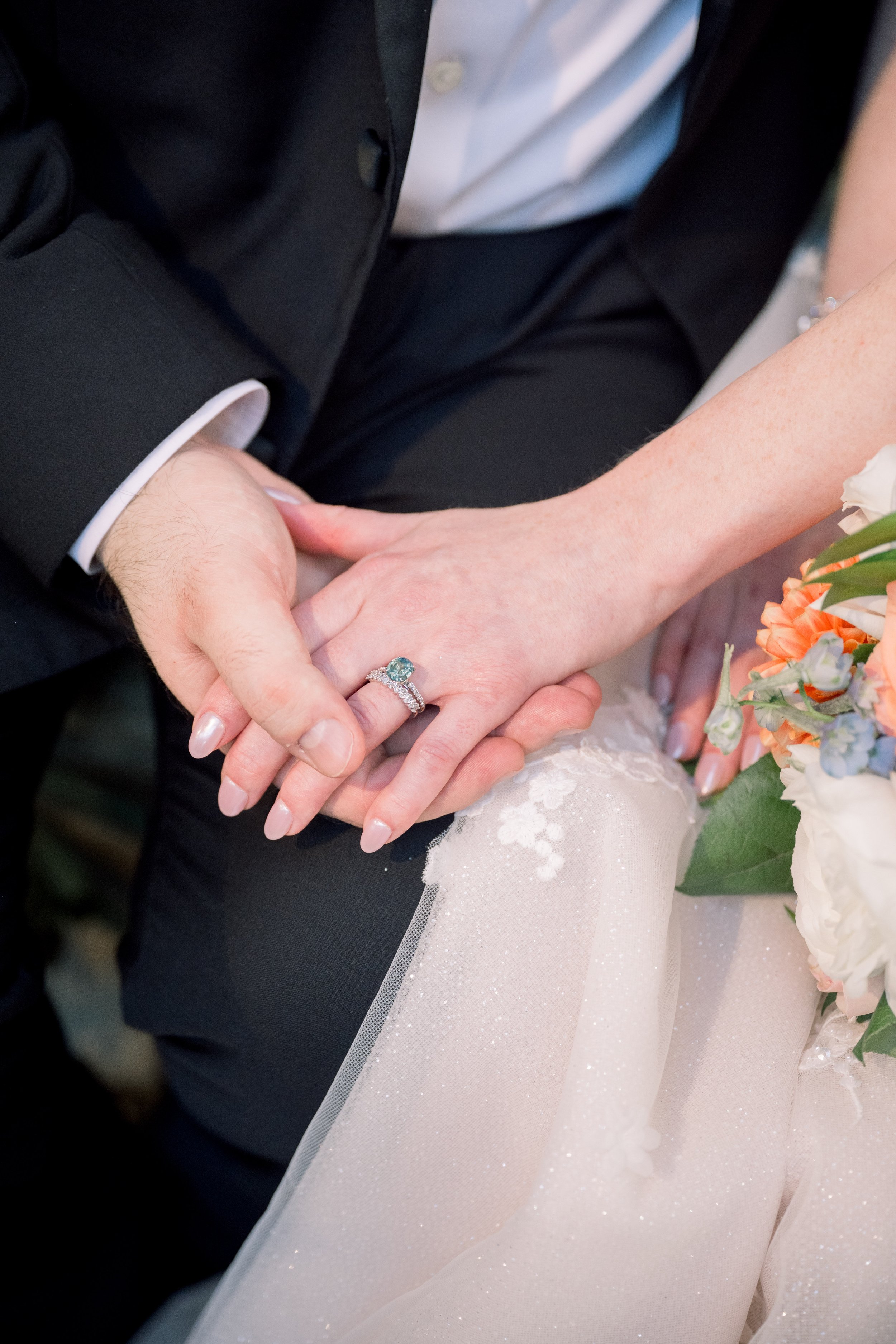 Close-up of the bride and groom holding hands with the bride’s engagement ring and bouquet visible