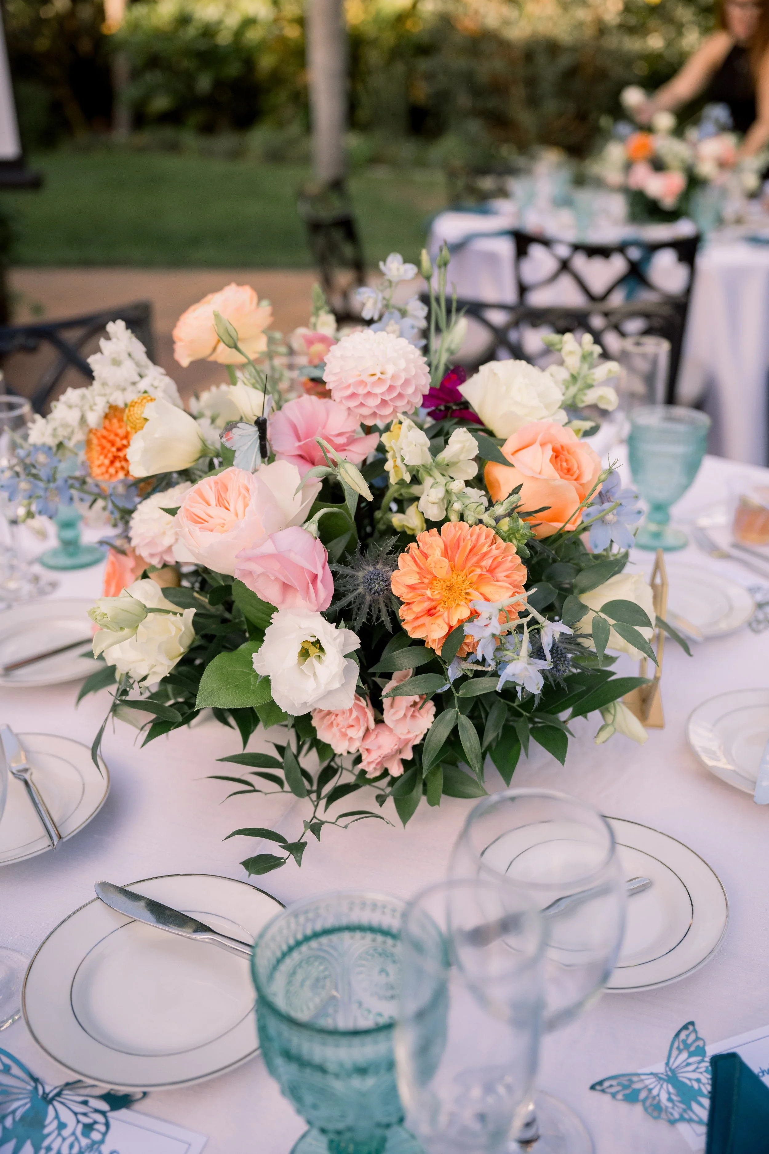 Colorful floral centerpiece with peach, blush, blue, and ivory blooms arranged on a wedding reception table