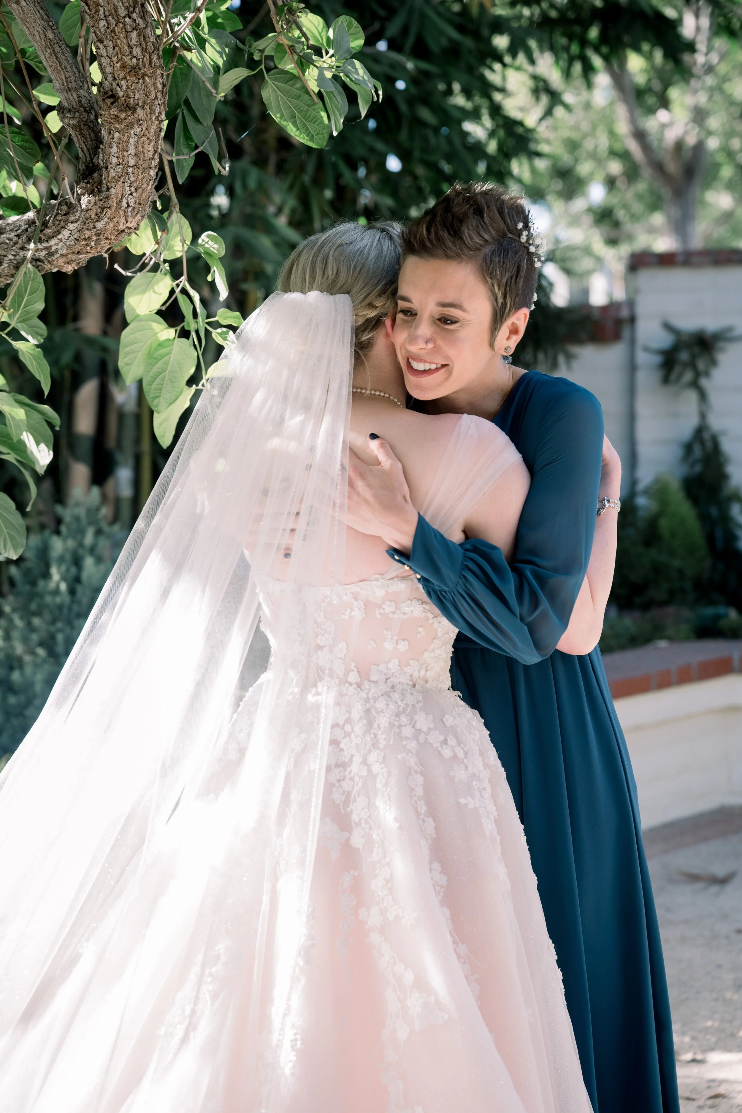 Bride embracing a smiling bridesmaid in a teal dress after an emotional first look before the wedding ceremony